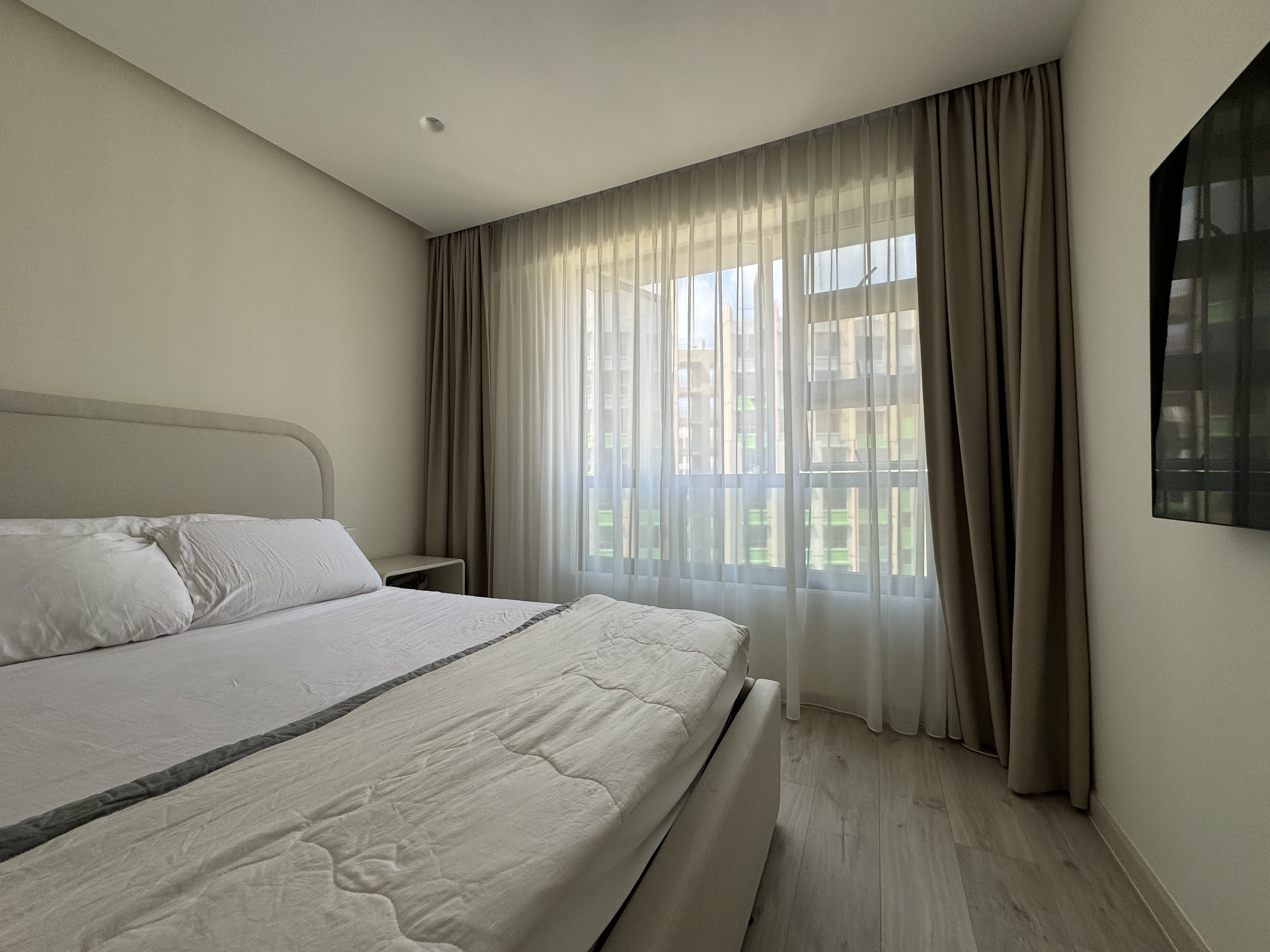 Cozy minimalist bedroom - Modern minimalist bedroom, neutral color palette, large bed with white linens, bedside table, sheer