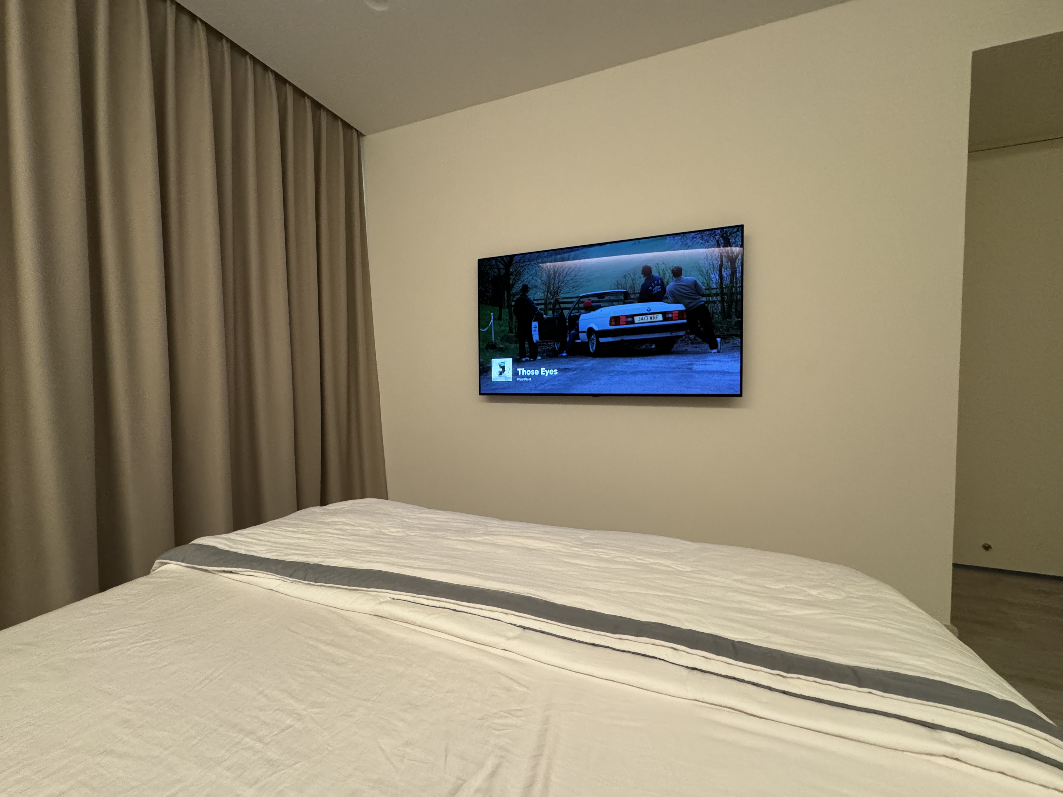 Cozy minimalist bedroom - Modern minimalist bedroom, beige curtains, sleek television, cozy bedspread, natural light