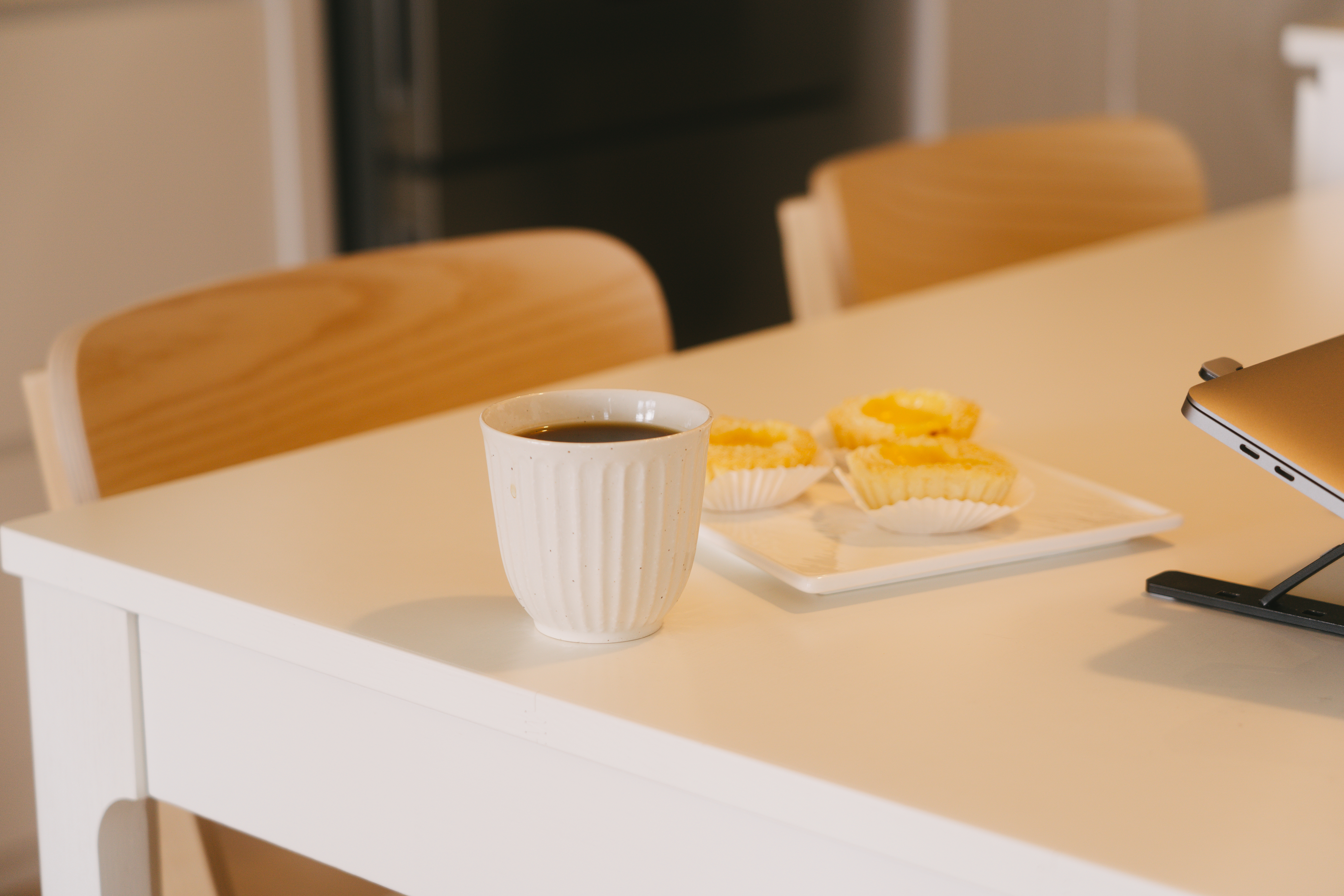 A place where food and conversations meet – Dining area - White table, modern kitchen, cup of coffee, wooden chairs, tray