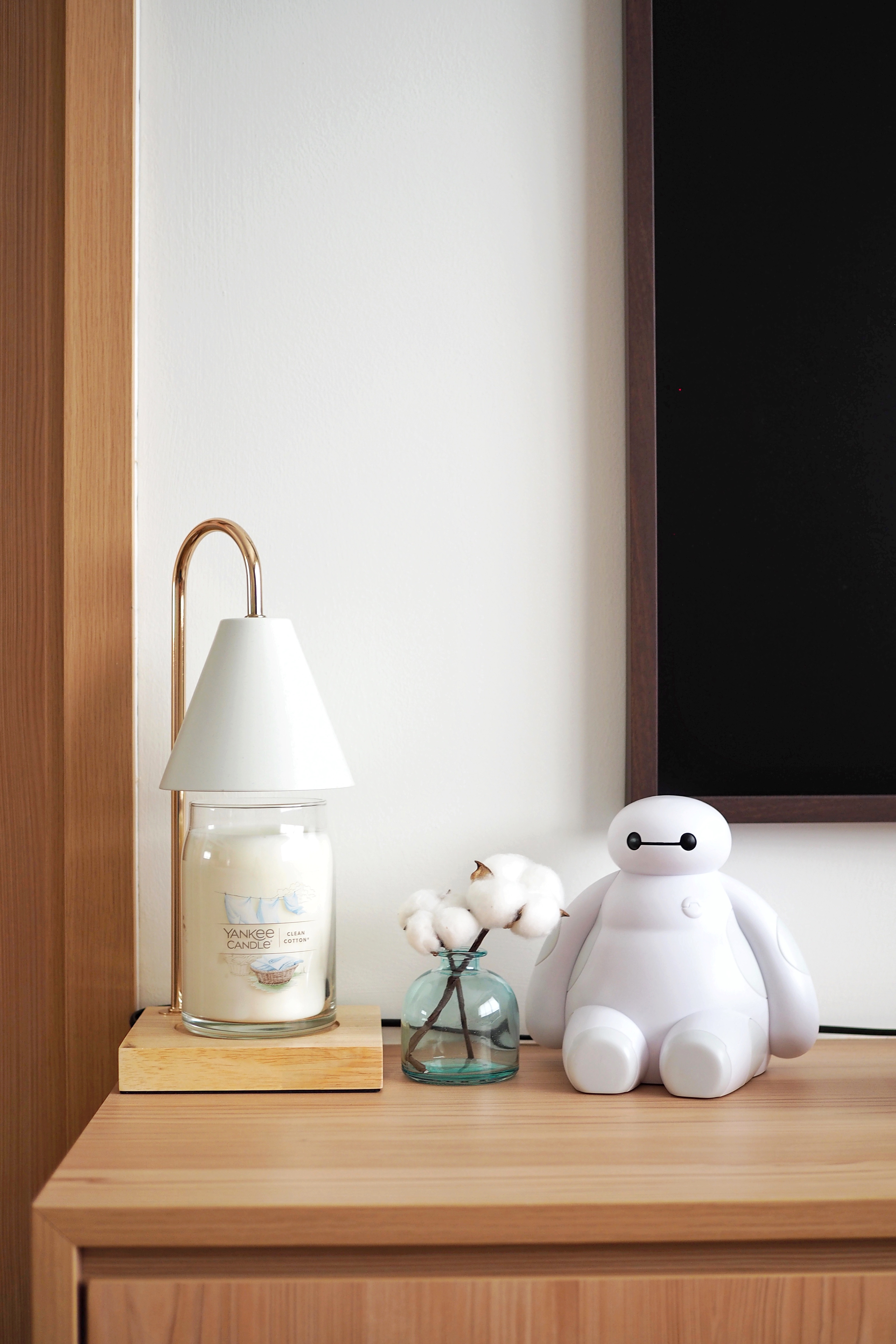 Minimalist home decor for a clutter-free home - White candle in glass jar, candle holder with gold finish, natural wood