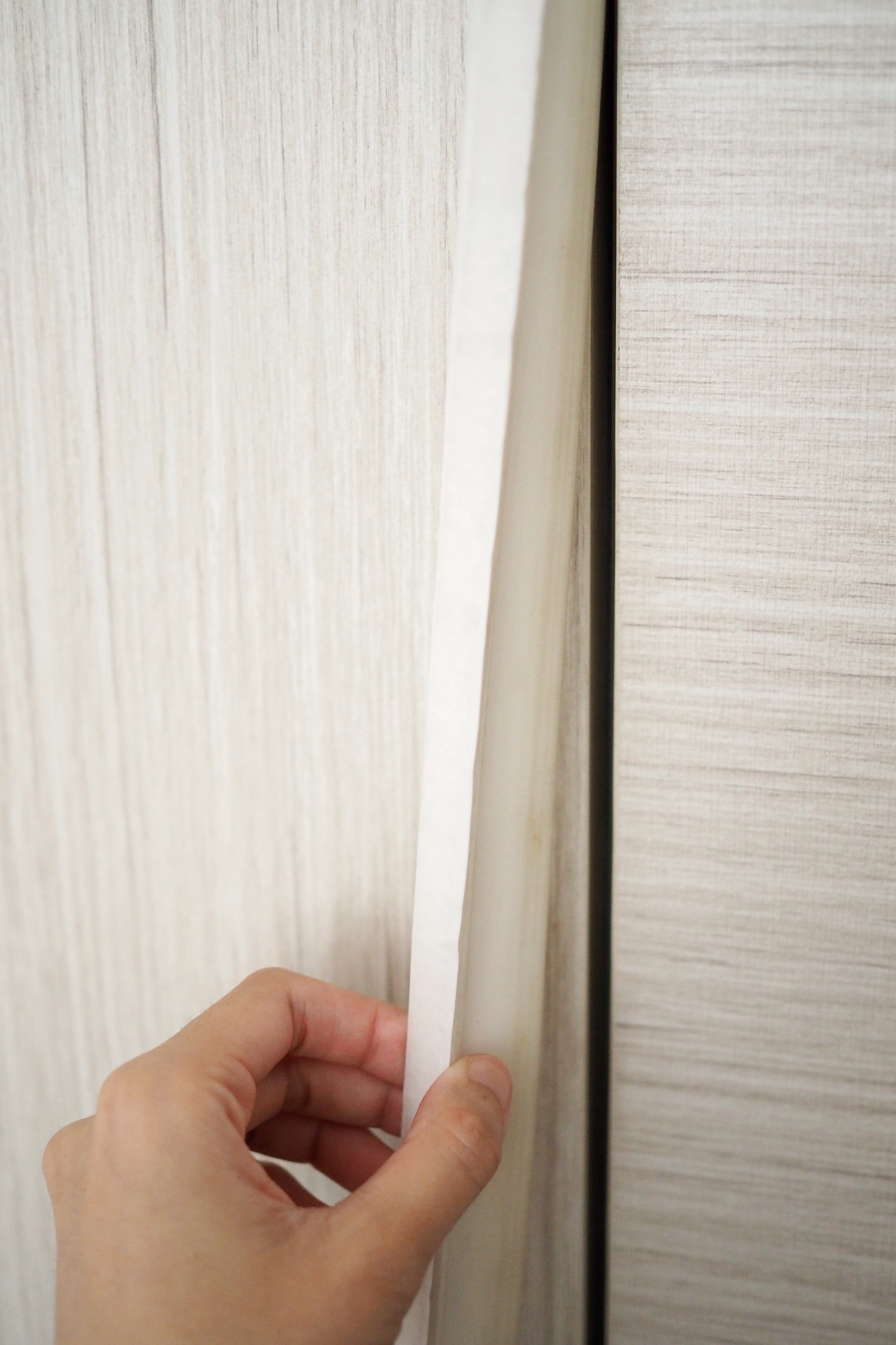DIY: Keeping dust, smoke and pests out of our house - Hand holding a white strip of paper, close-up view, textured wall