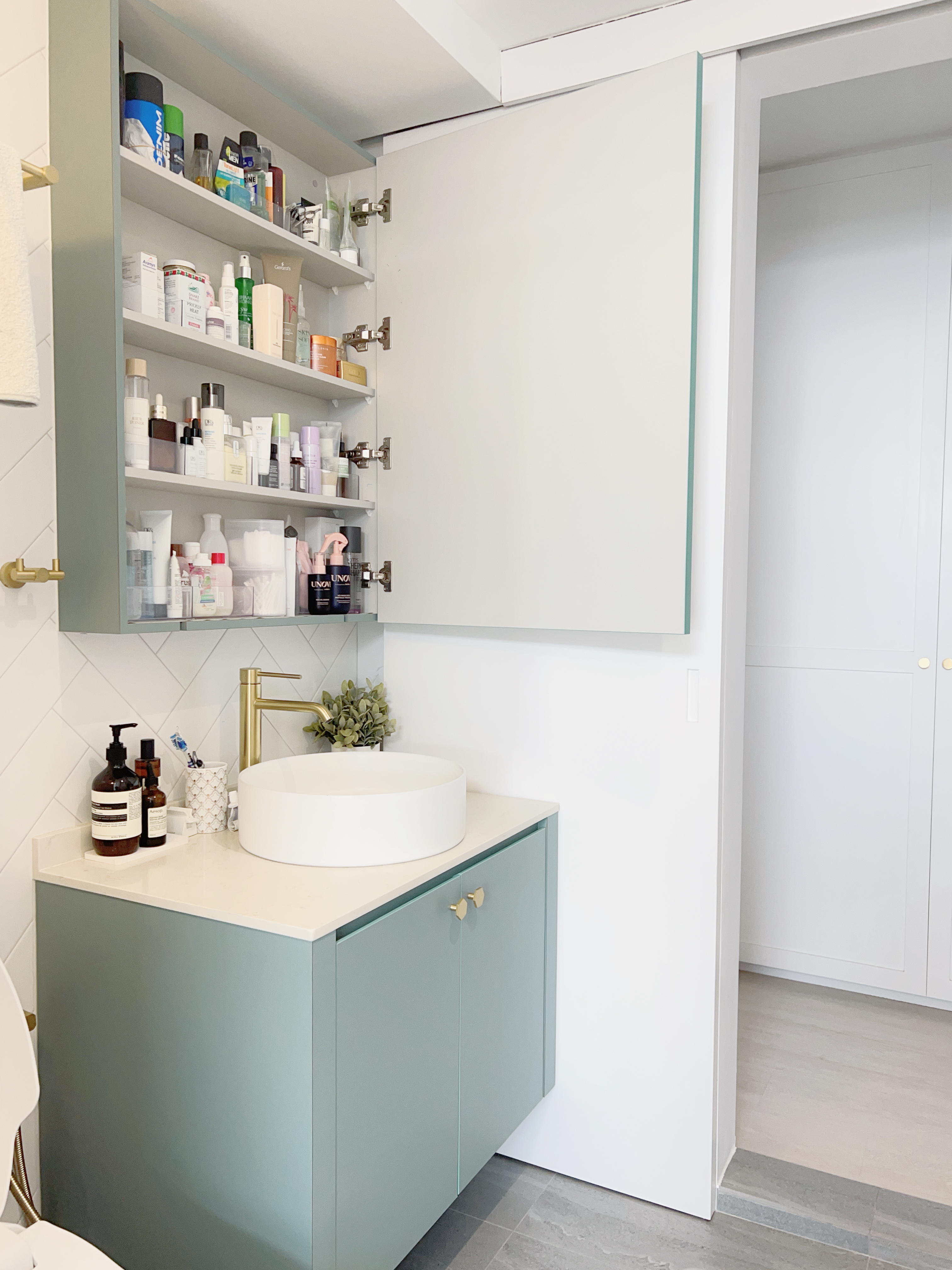 Two Bathrooms, Two Design Concepts! - Bathroom vanity with open medicine cabinet, white tiled wall, gold faucet, white