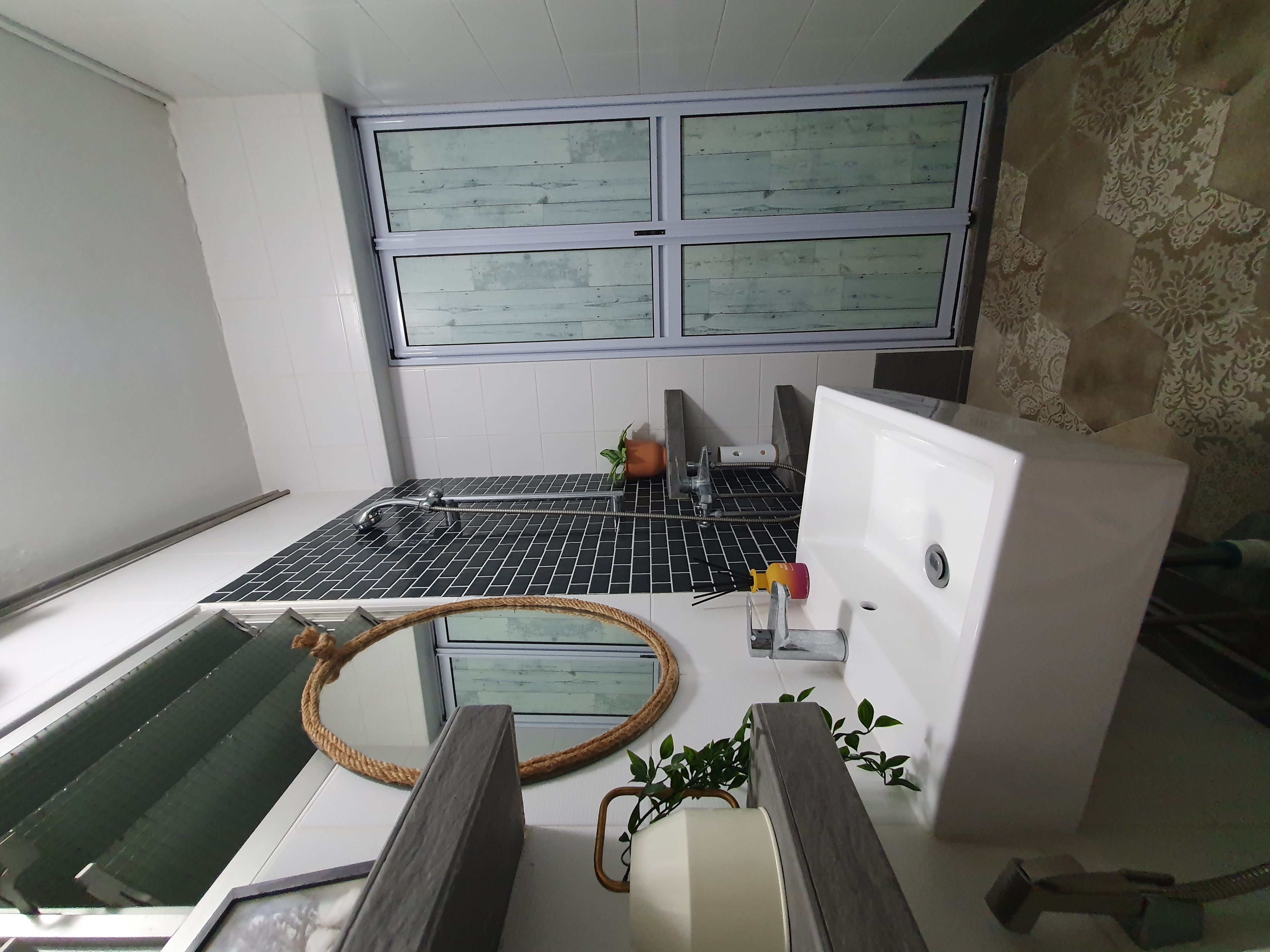 Unrenovated Bathroom - Bathroom vanity, white sink, black tiles, wooden paneling, window with frosted glass, green plants