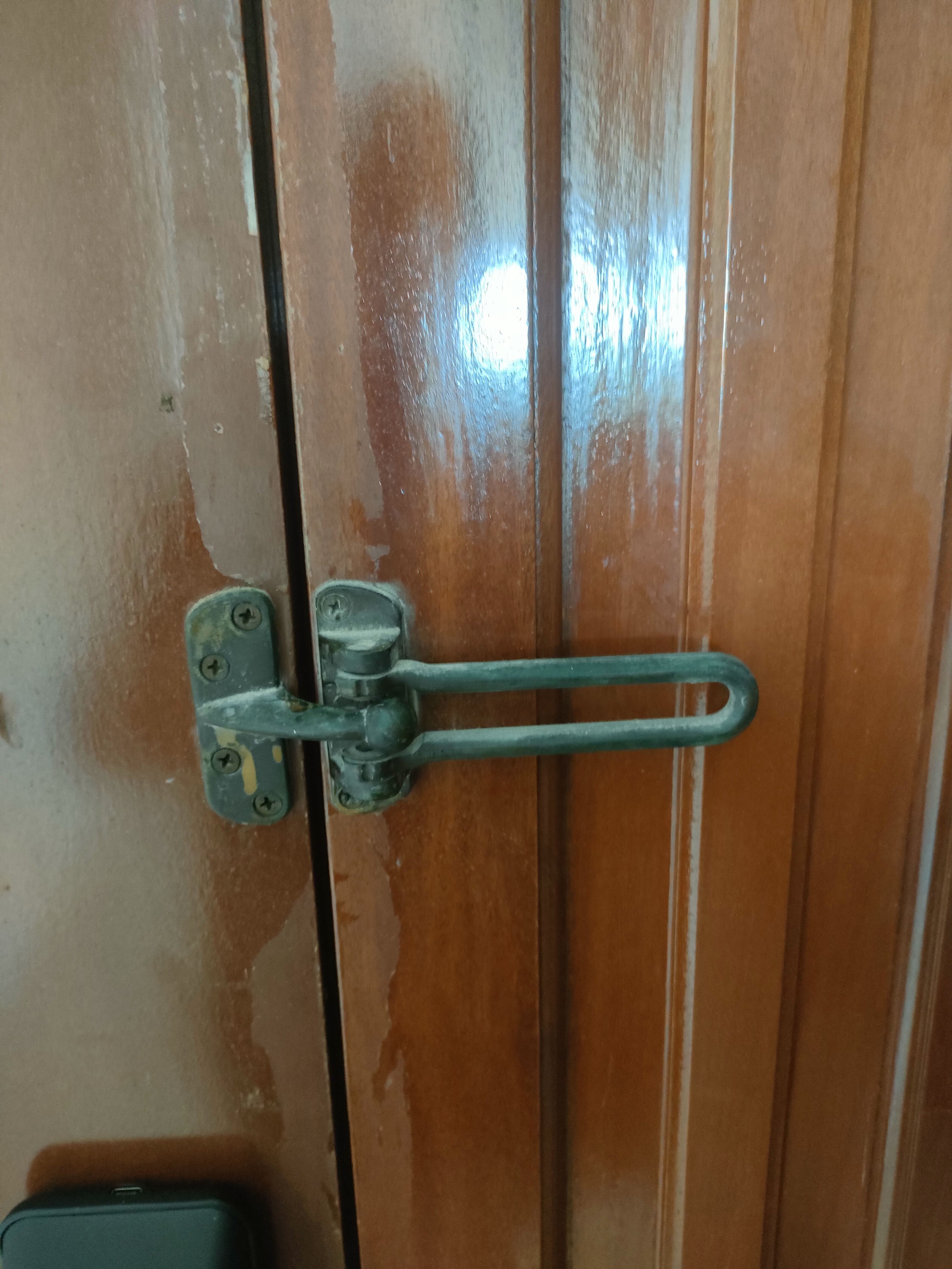 Our guests are greeted by this sight! - Wooden door with metal latch, slightly ajar, water droplets on door, brownish hue