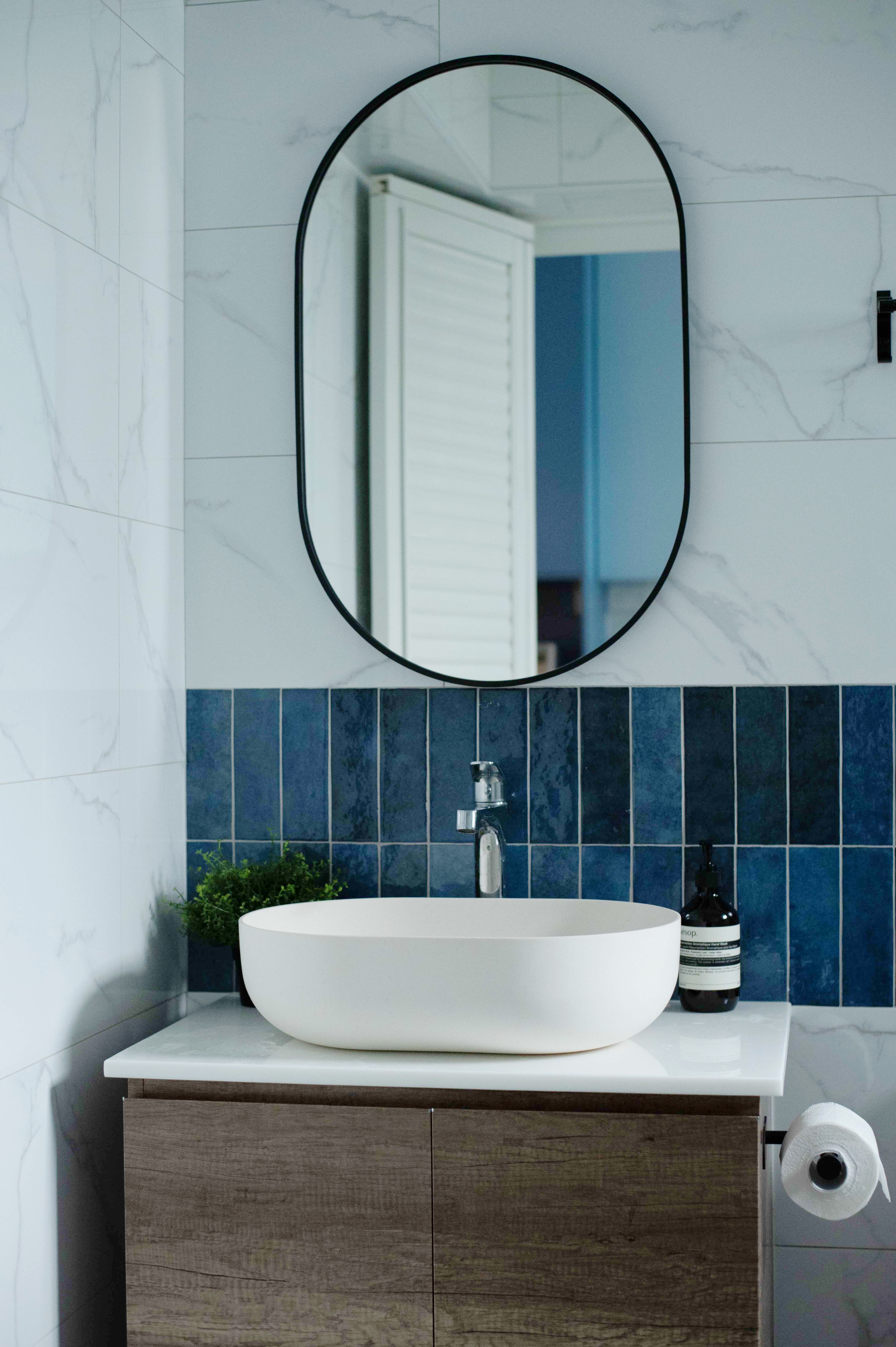 Exploring Blue Tones in a Scandinavian Home - Modern bathroom vanity, white sink, blue tiled backsplash, round mirror, wooden