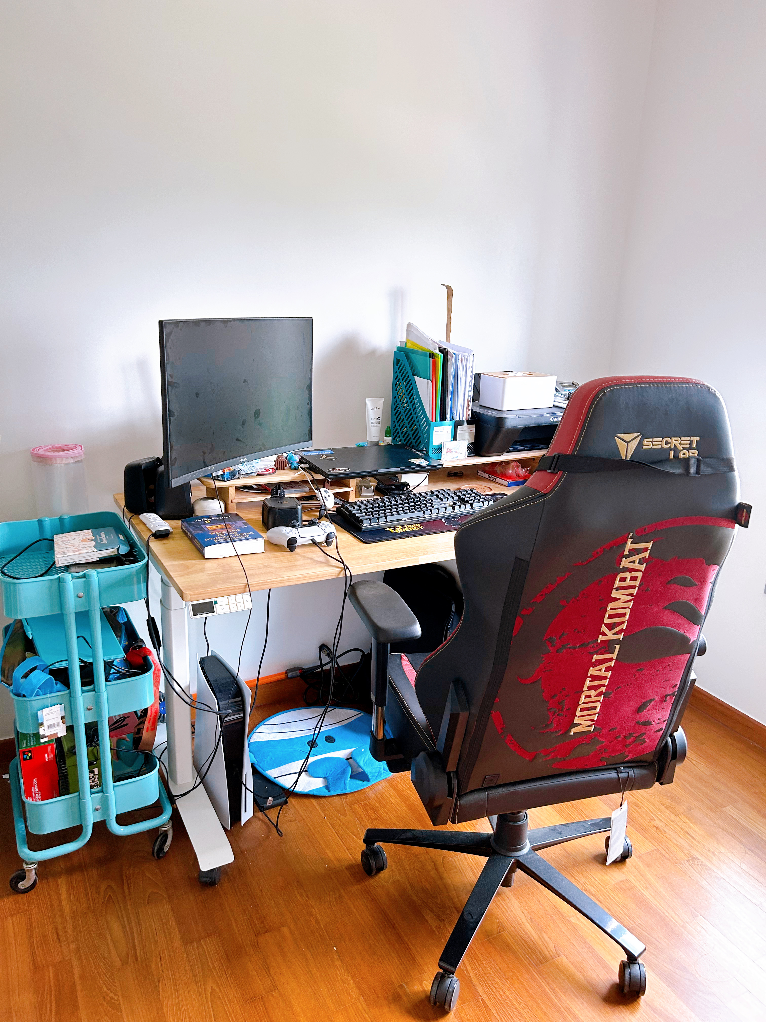 A study in a multi-functional room  - Desk with computer monitor, gaming chair labeled "Mortal Kombat, " keyboard, mouse