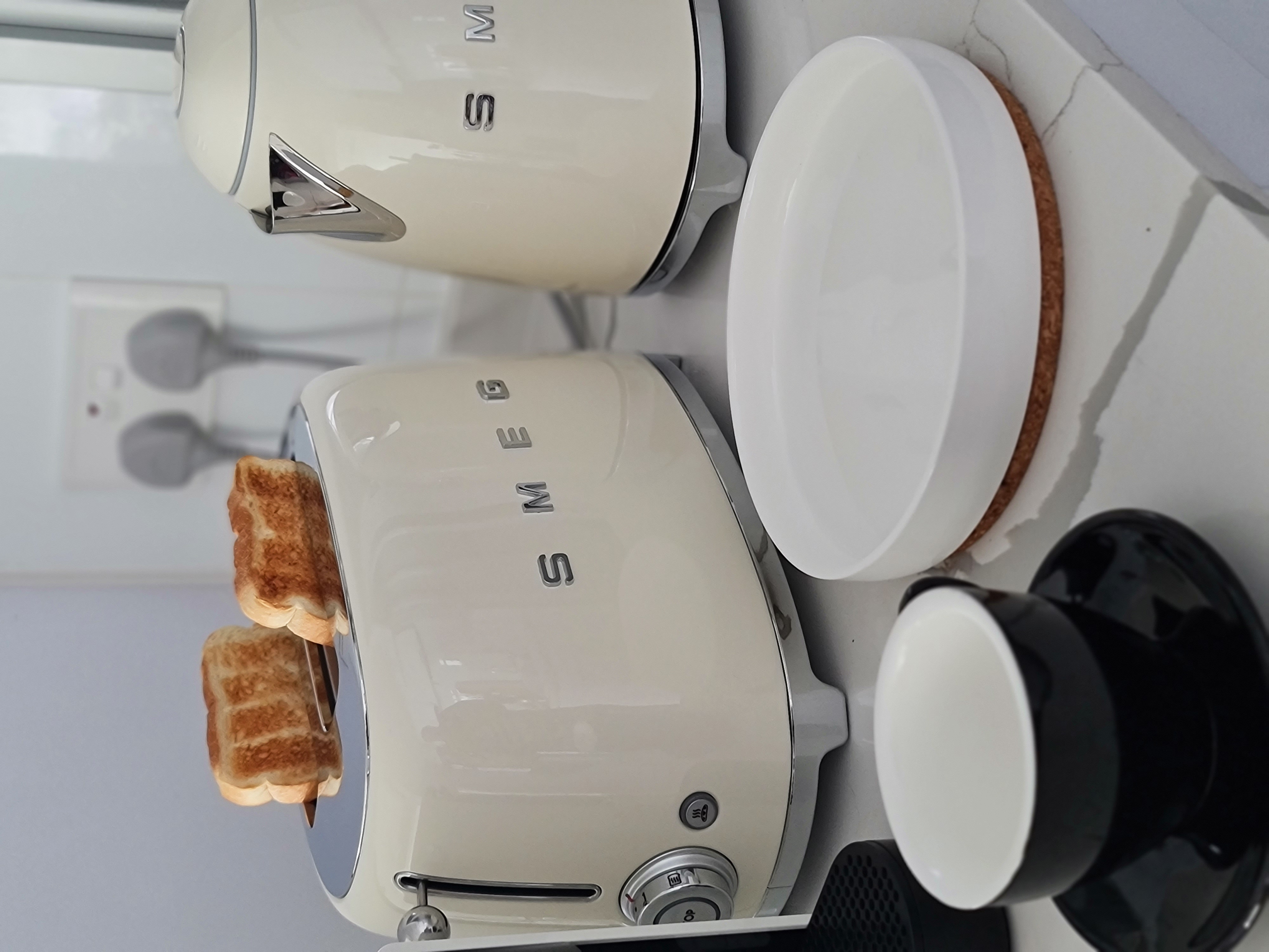 Enjoy your home, you deserve it! - White toaster with "SM" logo, two toasted bread slices, white plate with brown cake, black