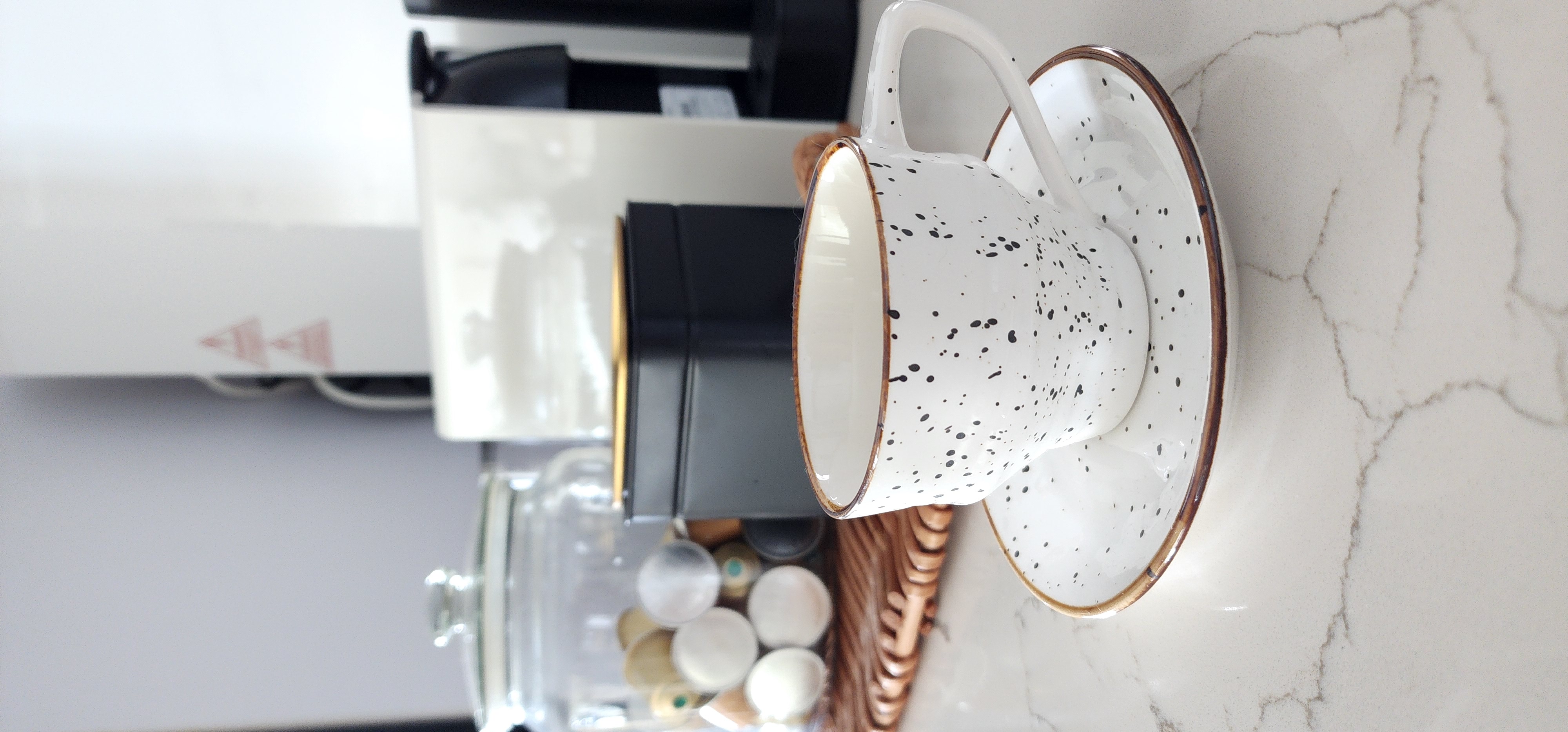 Enjoy your home, you deserve it! - White ceramic mug with black speckles, gold rim, modern kitchen countertop, coffee machine