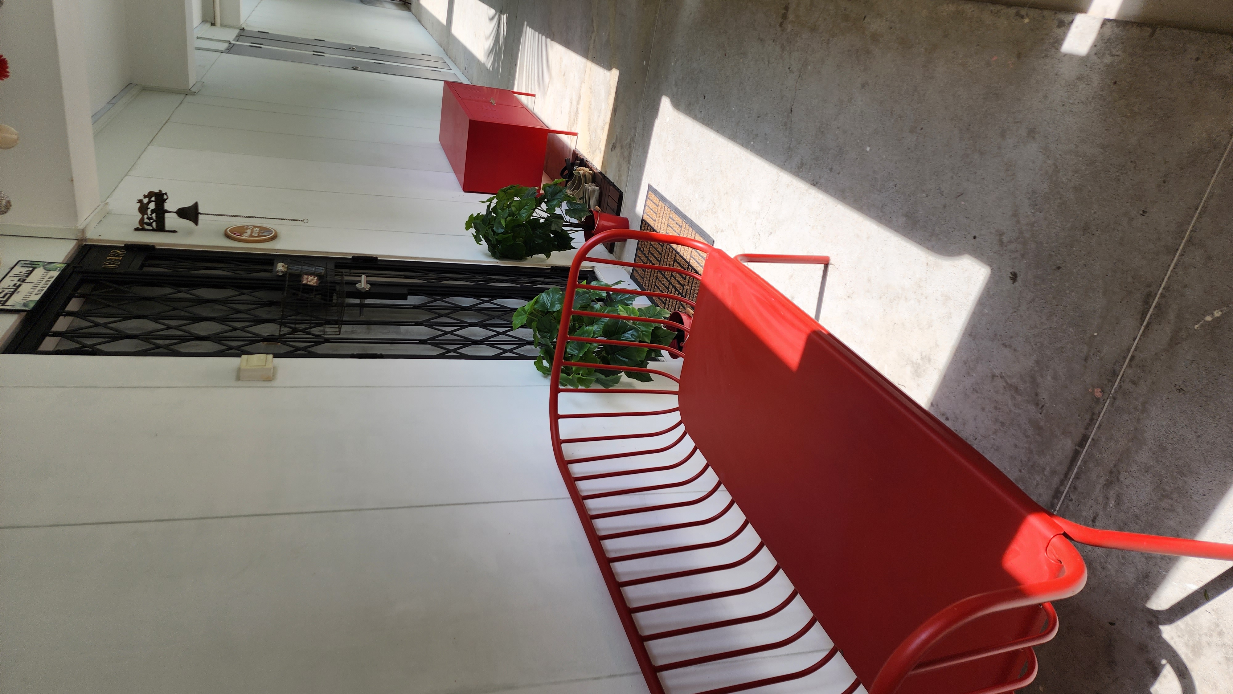 First Impression Matters - Entryway - Red metal chair, concrete floor, green plants, red chair rail, white wall, black metal