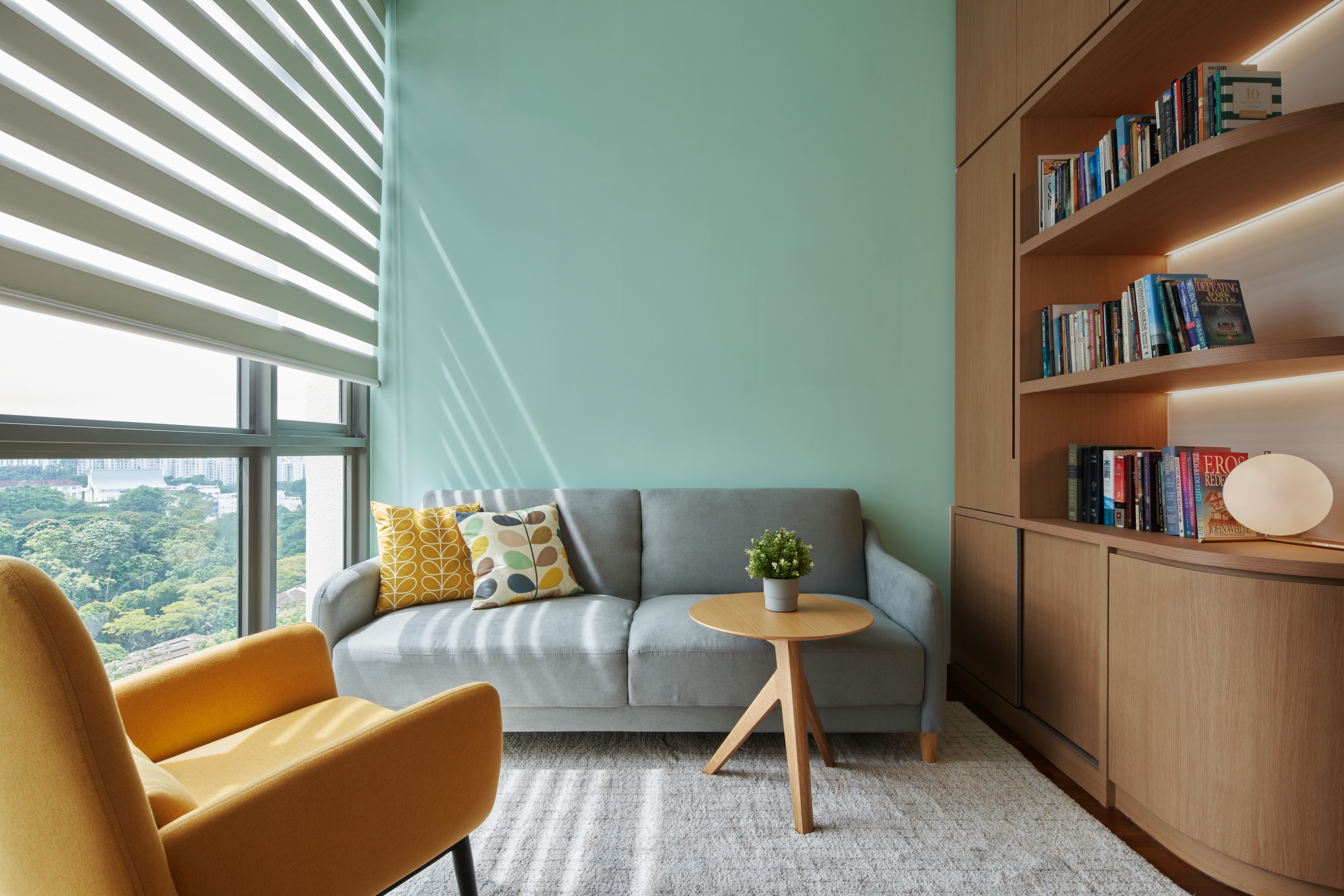 Crafting A Whimsical & Airy Home - Modern living room with large windows, light green walls, wooden bookshelf, gray sofa with