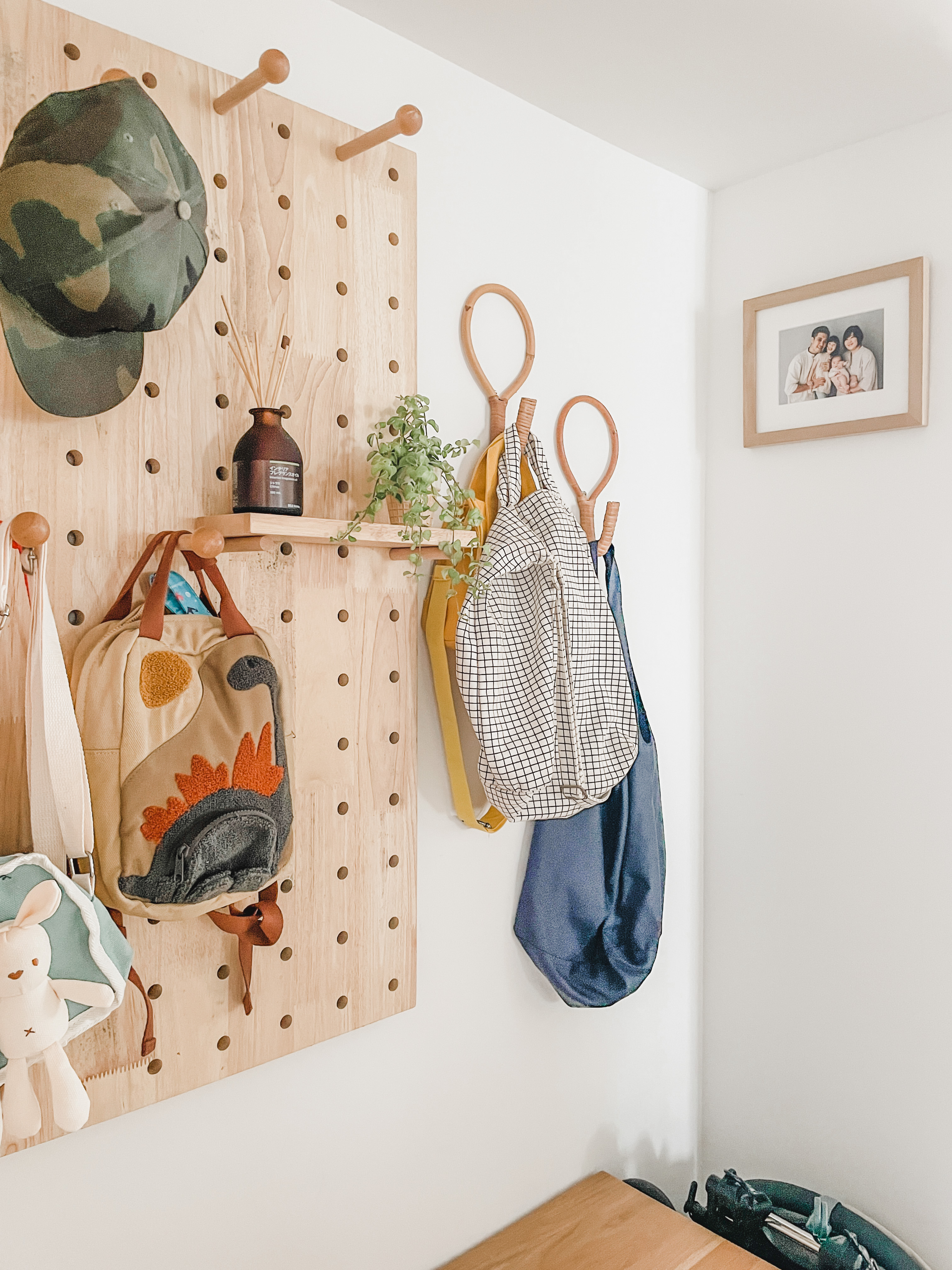 A Welcoming Entryway   - Wooden wall with various hanging items, camouflage hat, wooden hangers, potted plant, brown wooden