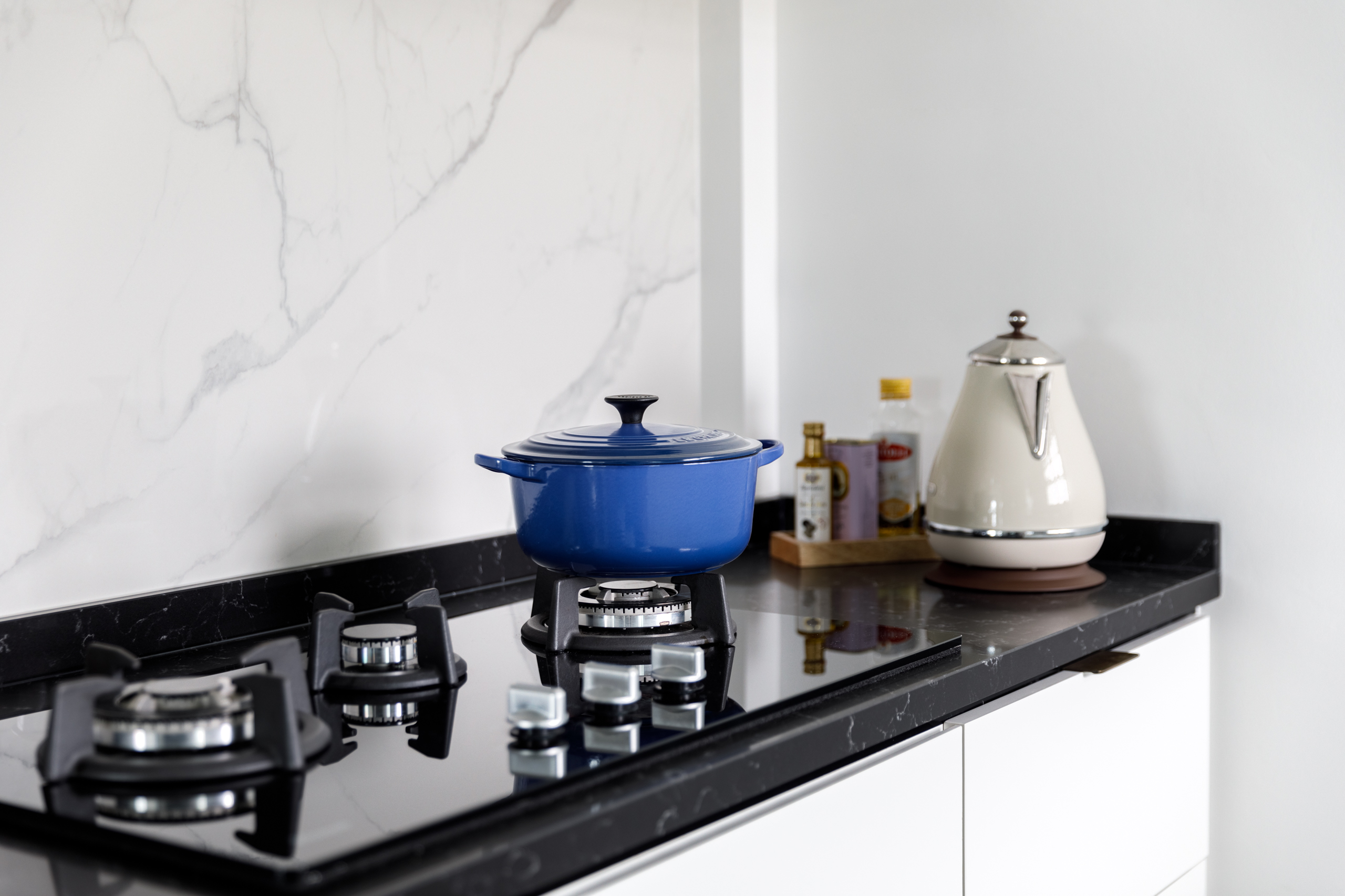A Minimalist & Industrial Look For A Young Couple - Marble backsplash, black countertop, blue pot on stove, modern kitchen
