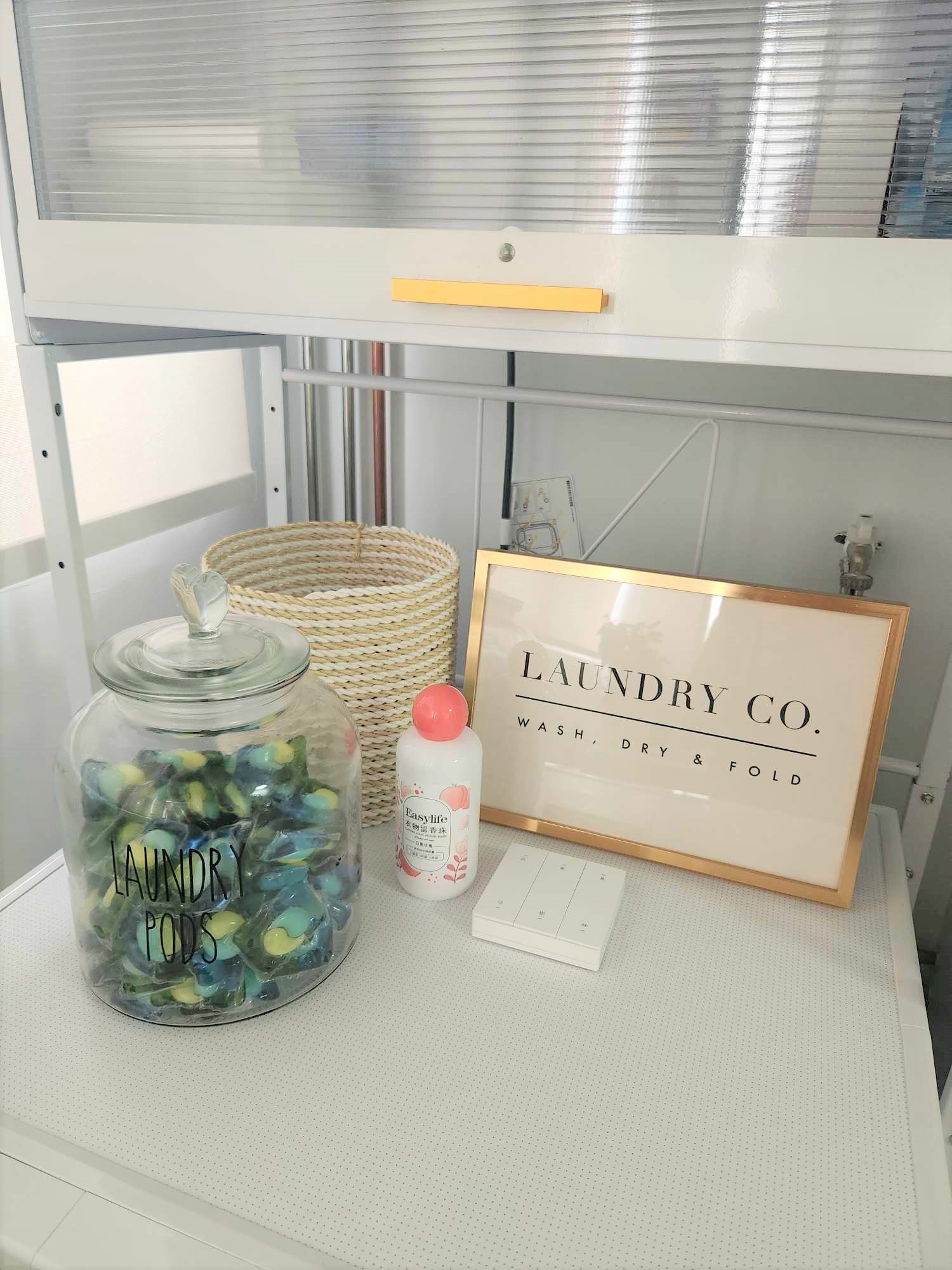 Our laundry space  - Laundry pods, glass jar, laundry detergent, white shelf, laundry detergent bottle, white frame, laundry