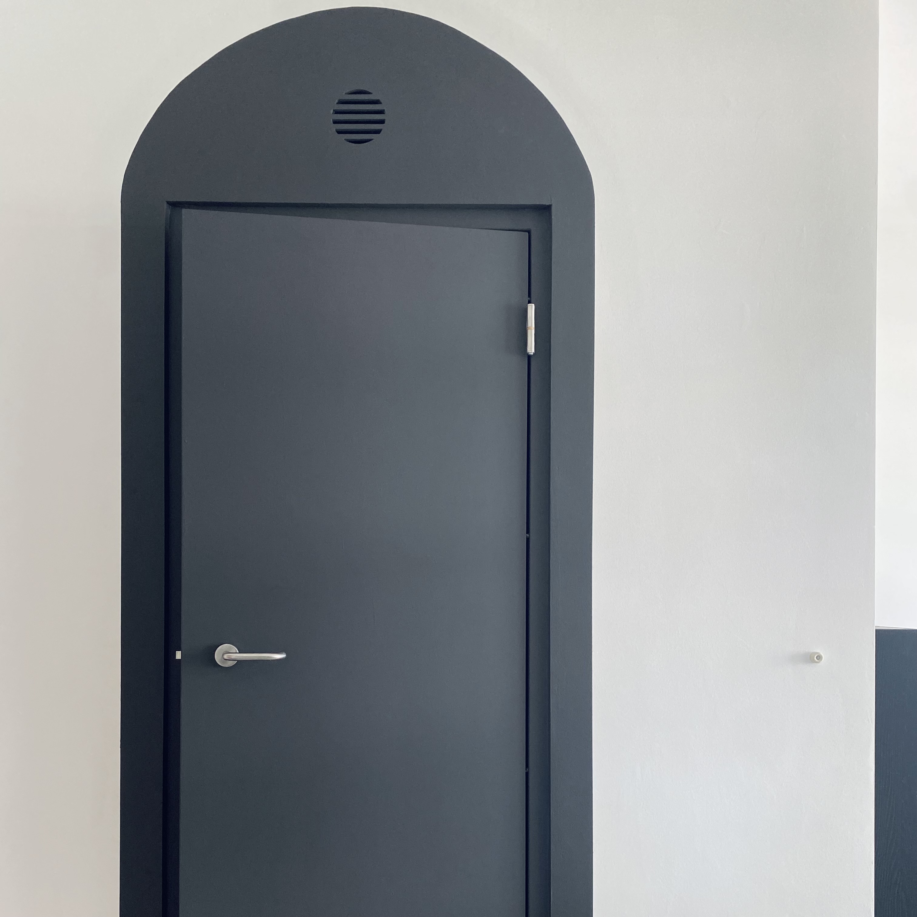 Entryway - cheap way to hide the ugly bomb shelter door! - Dark gray door with sleek handle and silver hinges, arched top