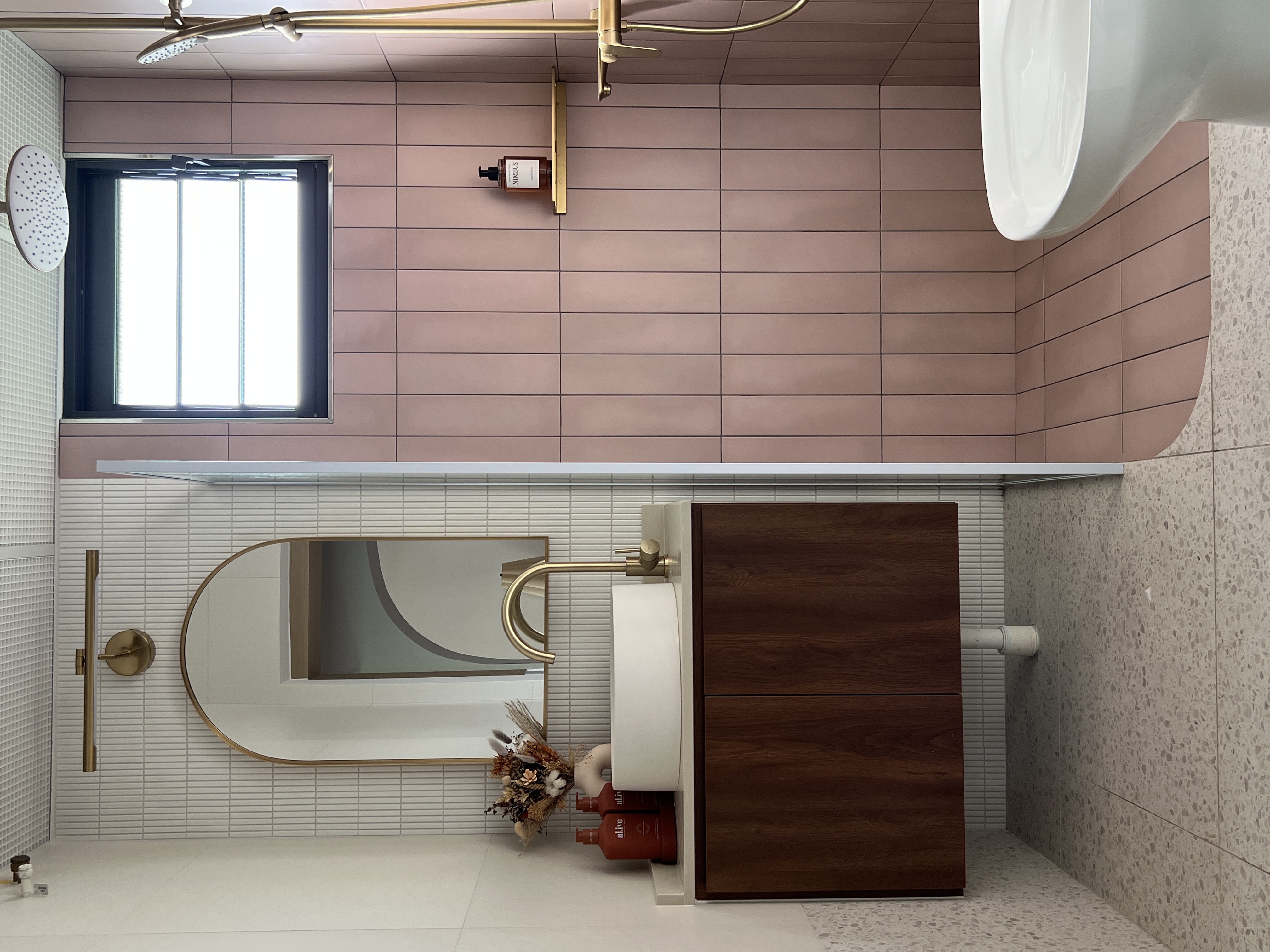 A mix of everything, with a bit of everything.  - Modern bathroom with pink tiles, gold fixtures, large mirror, wooden