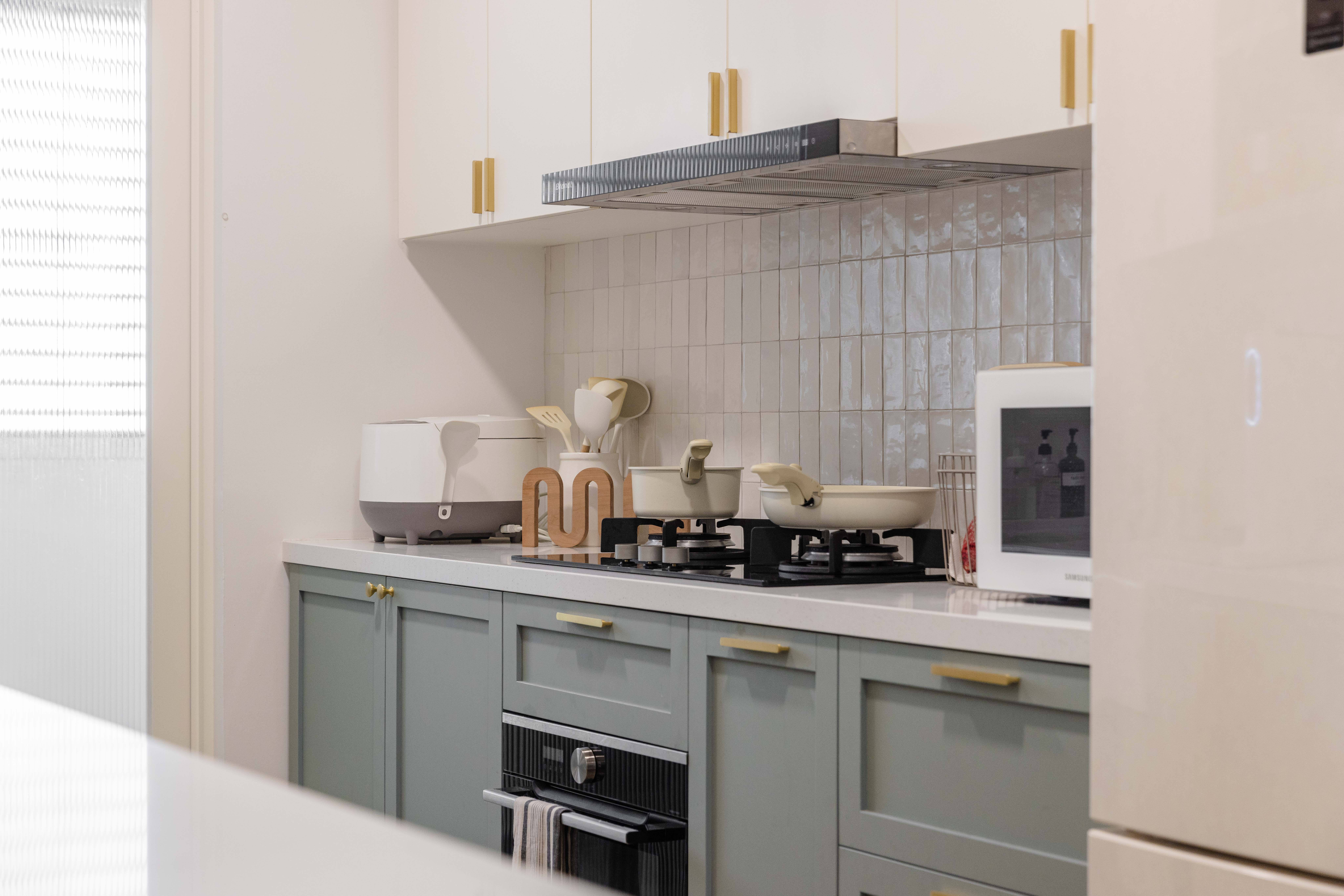 Bright, Airy & Curvy! - Modern kitchen with light grey cabinets and gold handles, stainless steel range hood, white tiled