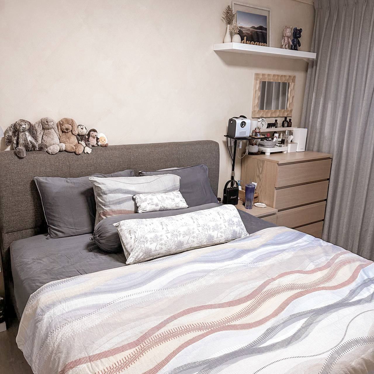 Bedroom Essentials - Grey bed with patterned bedding, plush toys on headboard, wooden nightstand, bedside table with a lamp