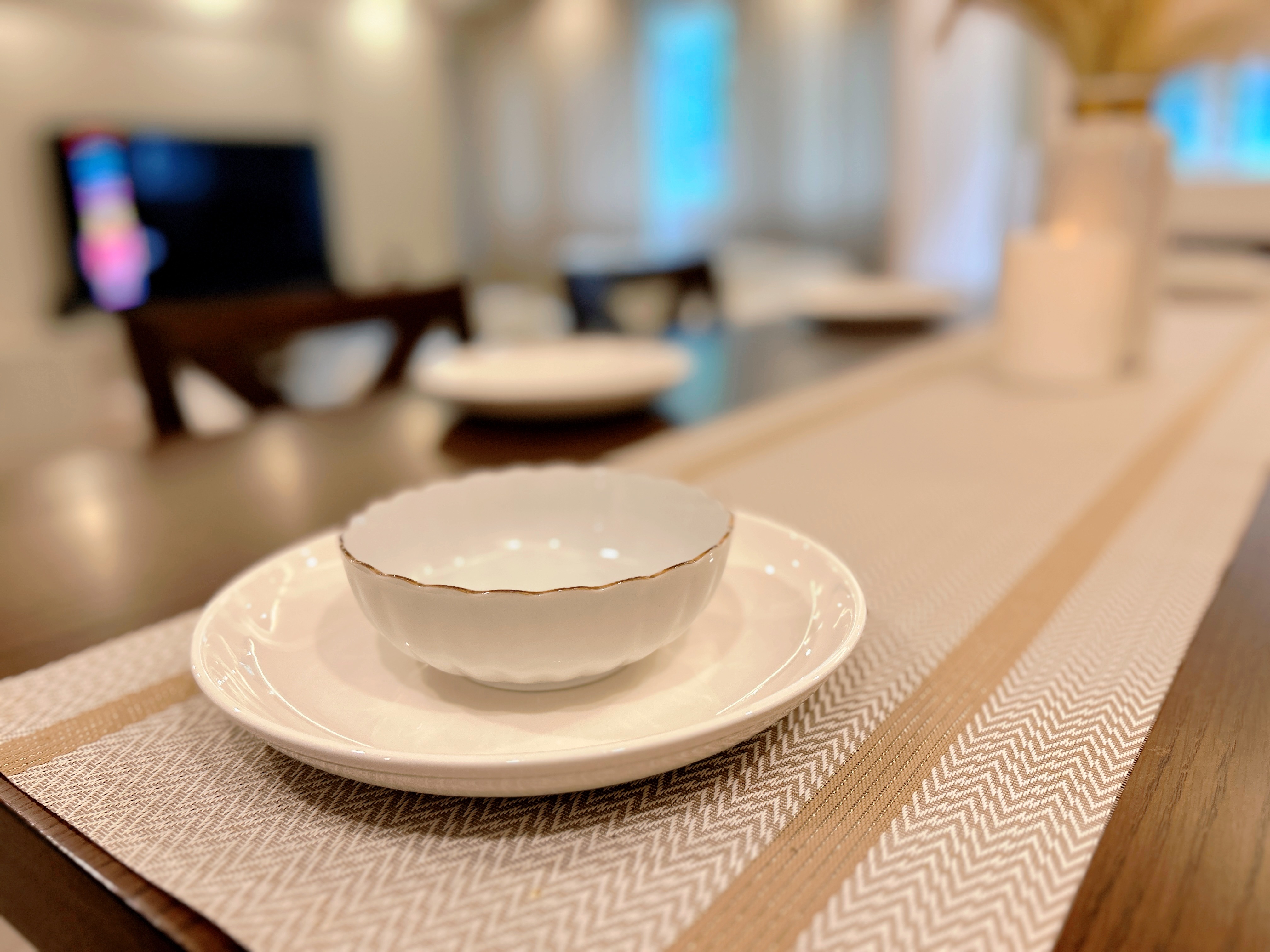 Our inviting dining space! - White ceramic bowl with gold rim, beige and brown patterned placemat, modern dining table, soft