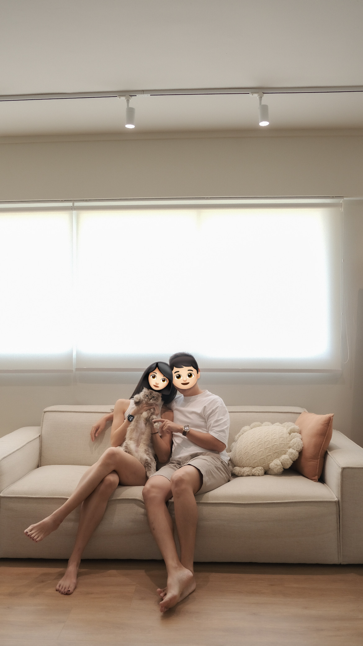 A calm and cosy space - Couple sitting on couch, pet cat, beige couch, light-colored walls, soft lighting, natural light