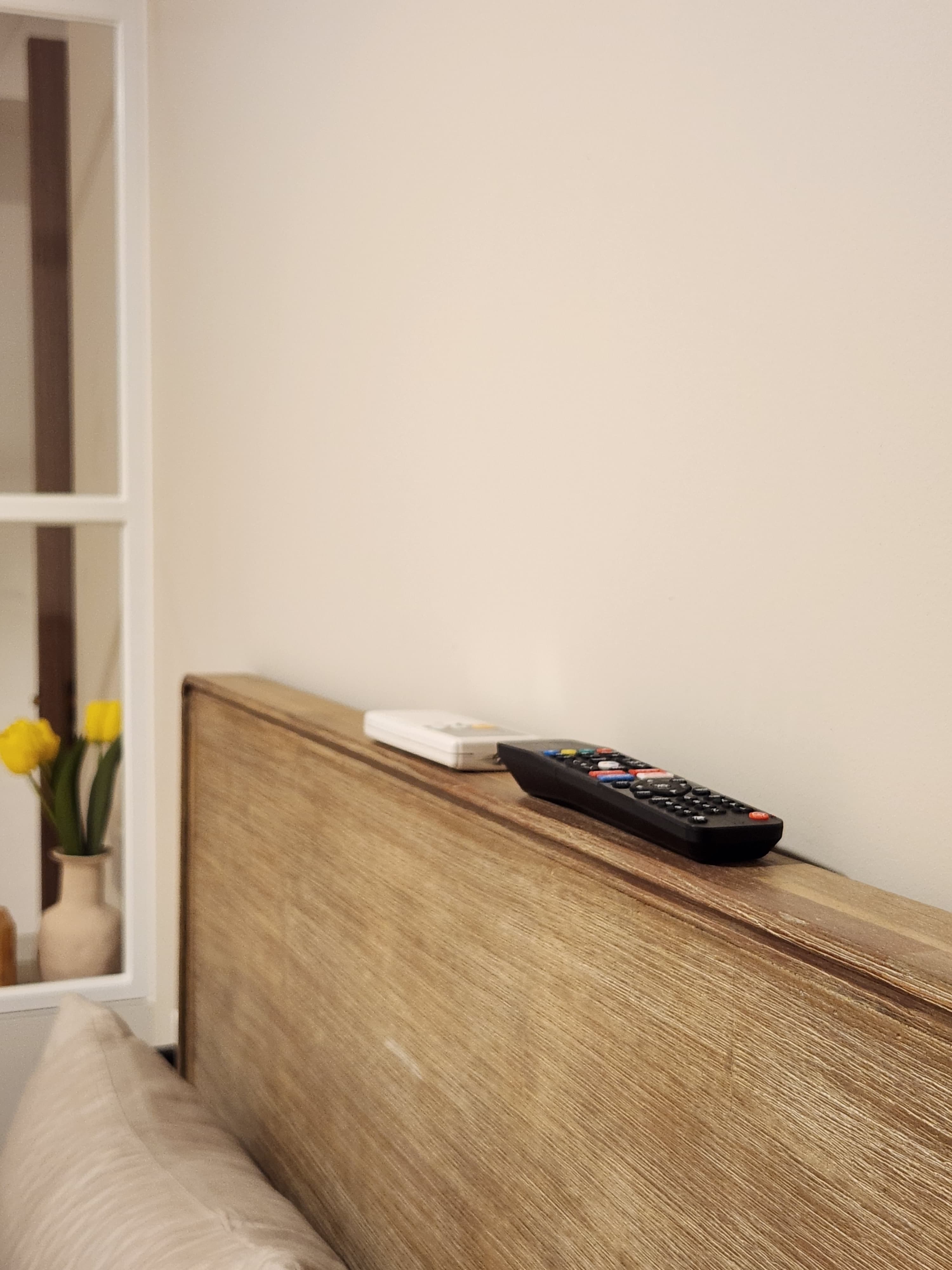 Restful Retreat in Our Neutral-Toned Master Bedroom - Wooden headboard, yellow tulips, white remote control, beige pillow