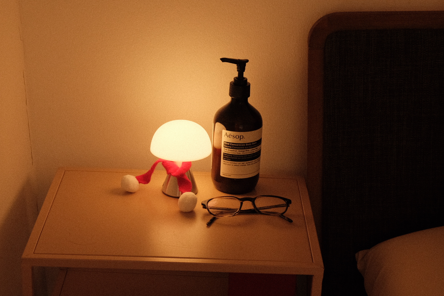 Our compact bedroom layout and accessories  - Lamp with glowing white bulb, wooden bedside table, pair of glasses, bottle of
