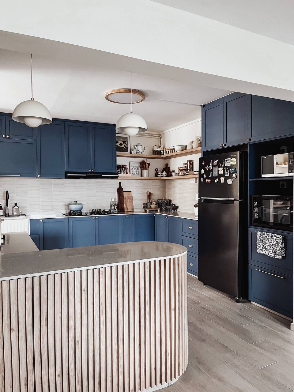 Blu Kitchen - Modern kitchen with blue cabinetry, sleek black refrigerator, wooden island countertop, pendant lights, white