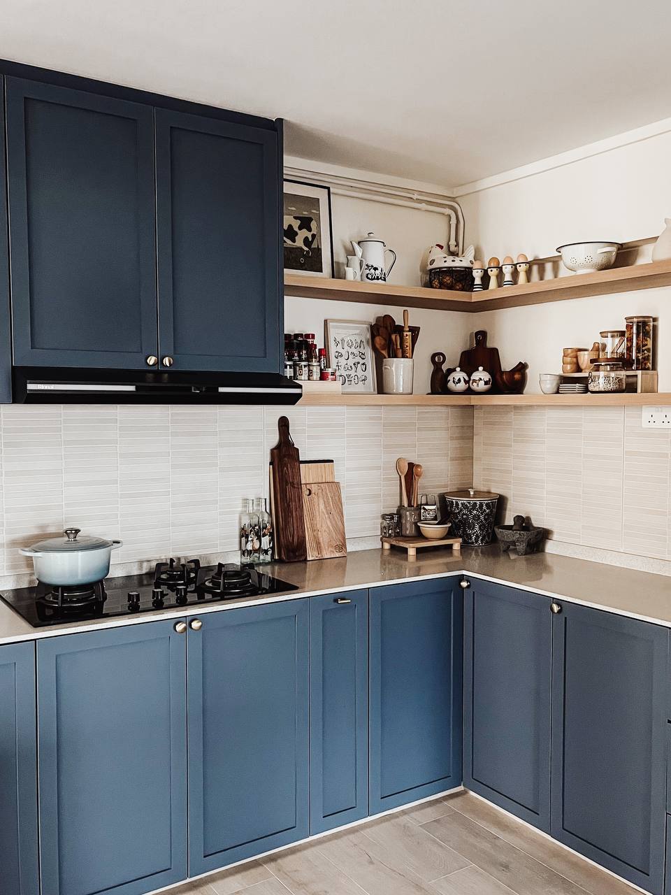 Blu Kitchen - Dark blue kitchen cabinets, white tiled backsplash, black range hood, gas stove with blue pot, wooden cutting