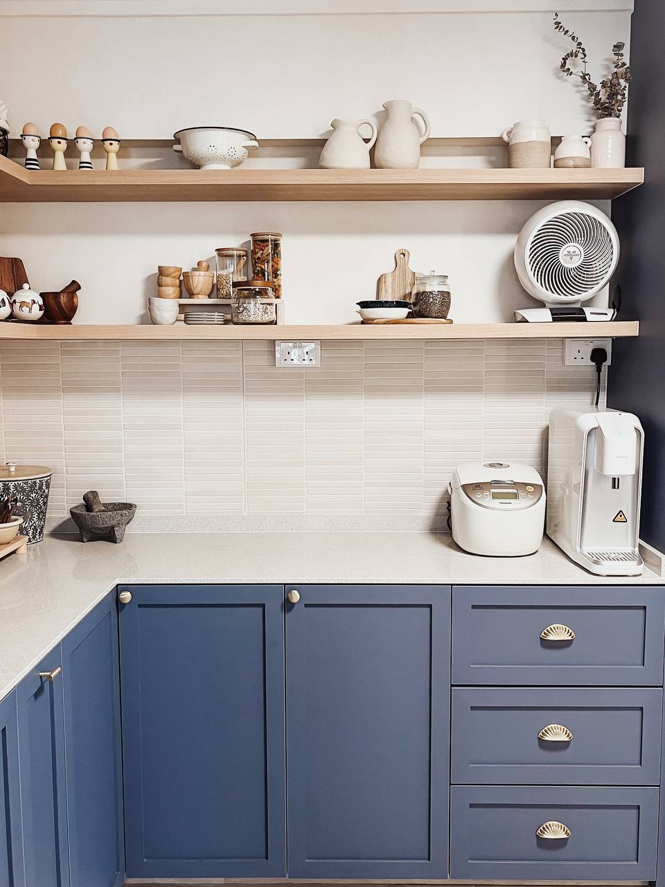 Blu Kitchen - Wooden kitchen shelves, blue cabinets, white tiled backsplash, white electric fan, ceramic utensils, wooden