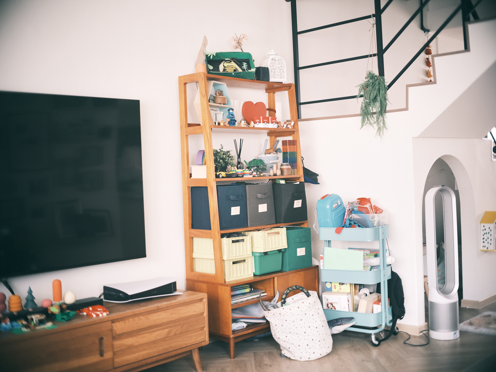 A relaxing mid-century family lounge area - Wooden shelving unit, black storage bins, colorful toys, green plant, white