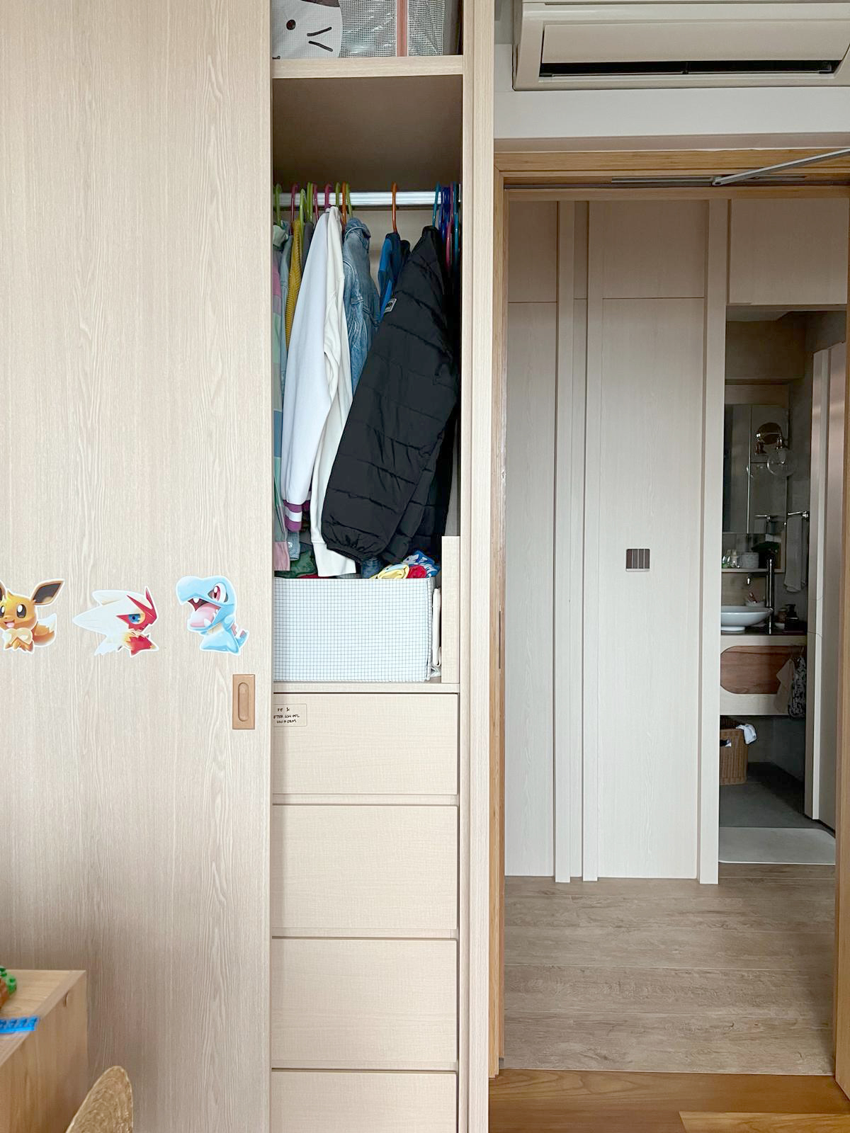 Reorganised Kid's Room  - Wooden wardrobe, open closet, clothes hanging, black jacket, white shirt, colorful clothes, cartoon