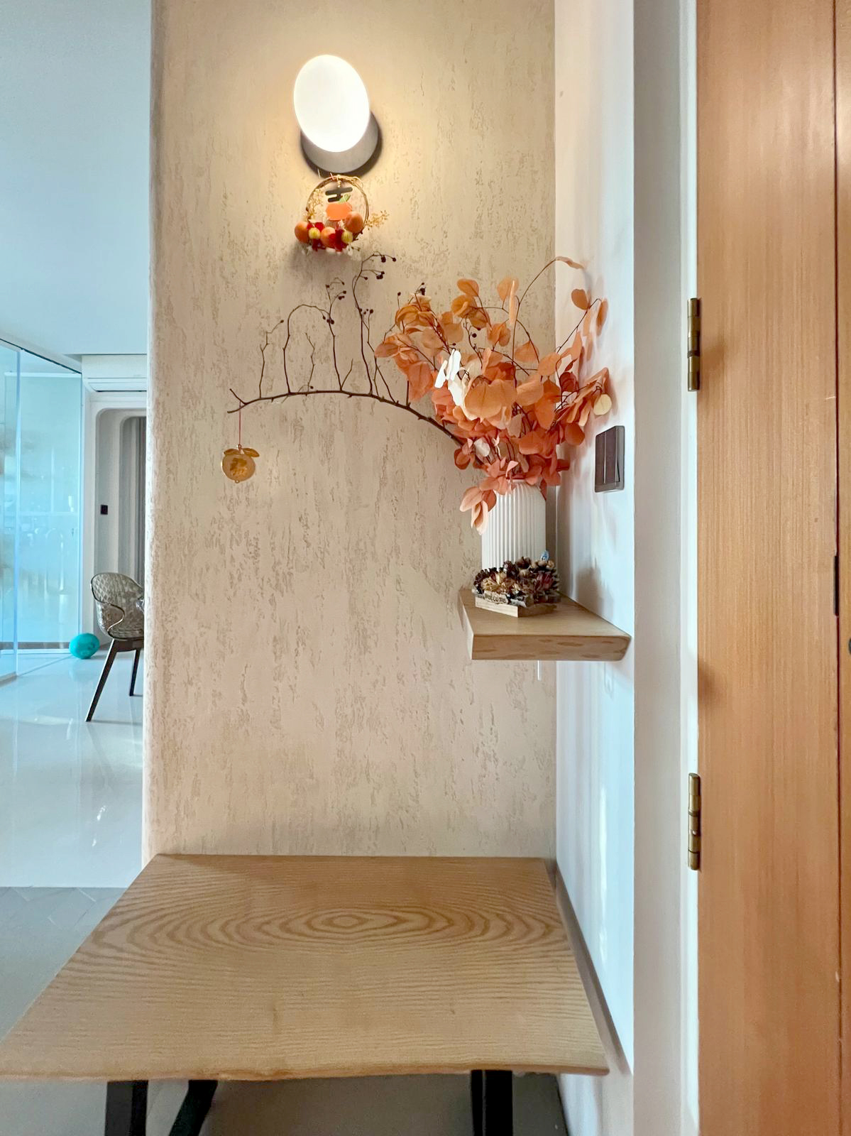 Our version of CNY deco  - Wall-mounted light fixture, textured beige wall, decorative fruit basket, autumn-themed vase