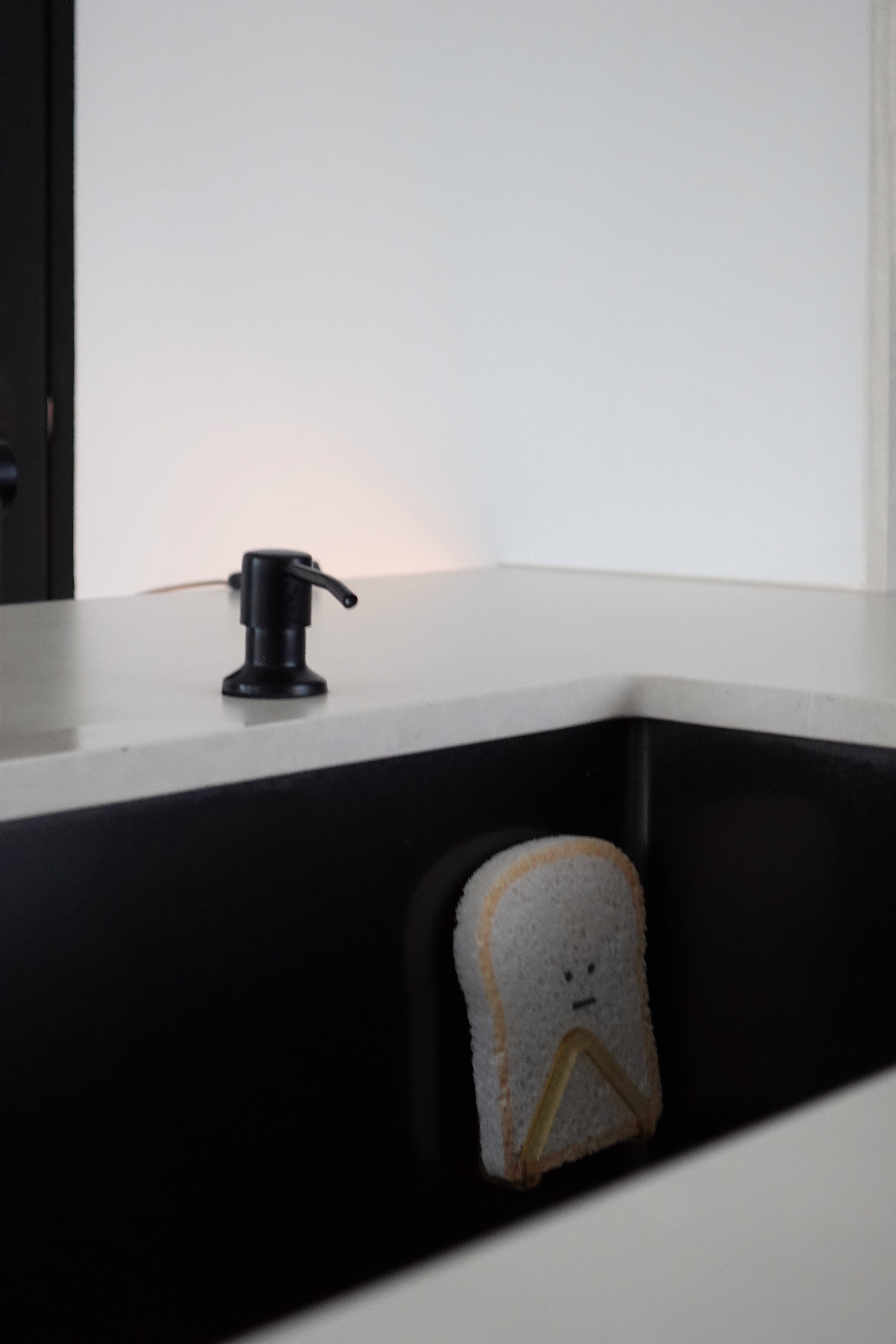 How we hid everything for a minimal kitchen - sink, sponge, black countertop, white wall, minimalist design, black faucet