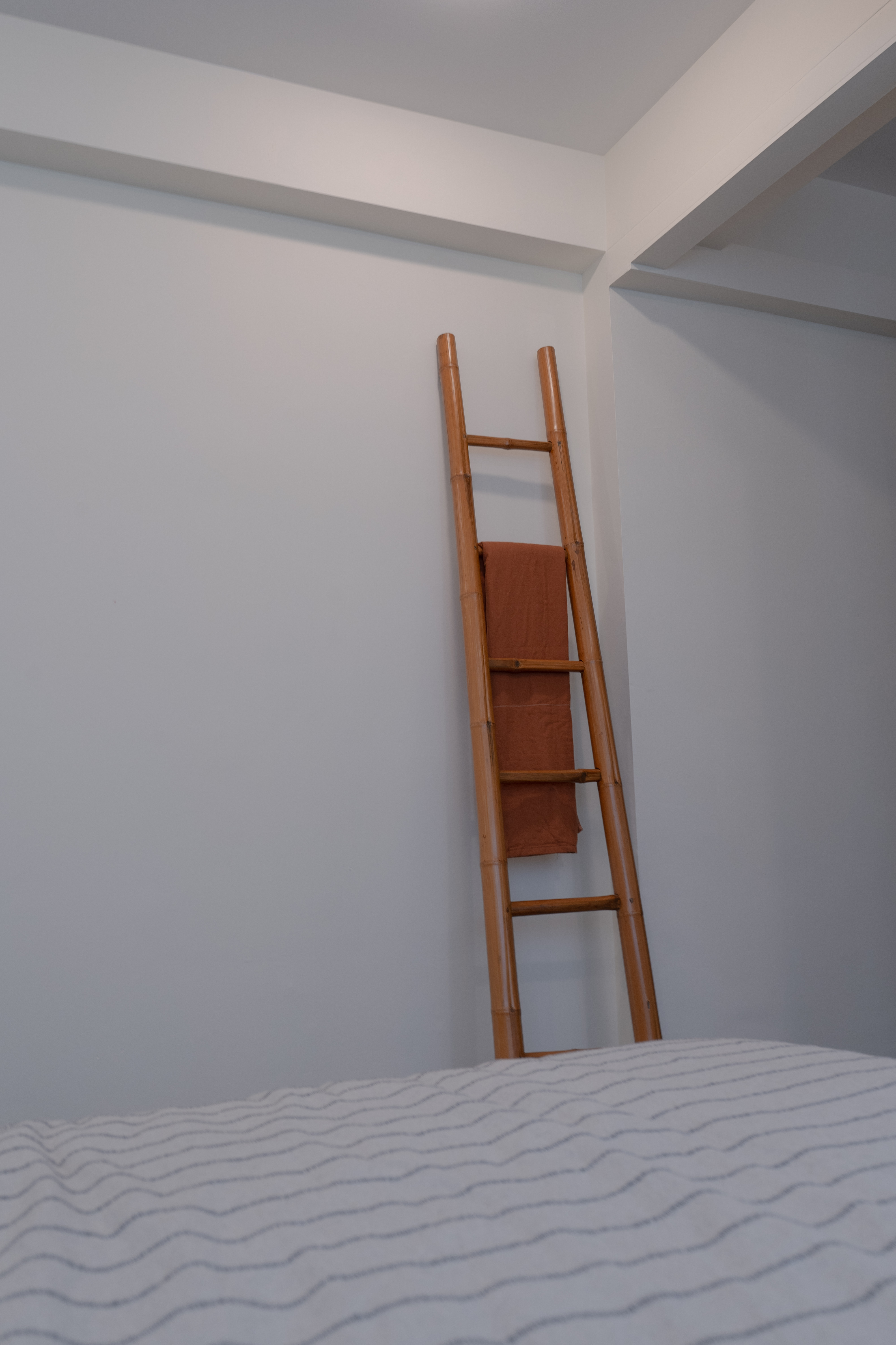 Resort-vibes Master Bedroom - Ladder against white wall, wooden ladder, orange towel, white bedspread, wavy pattern