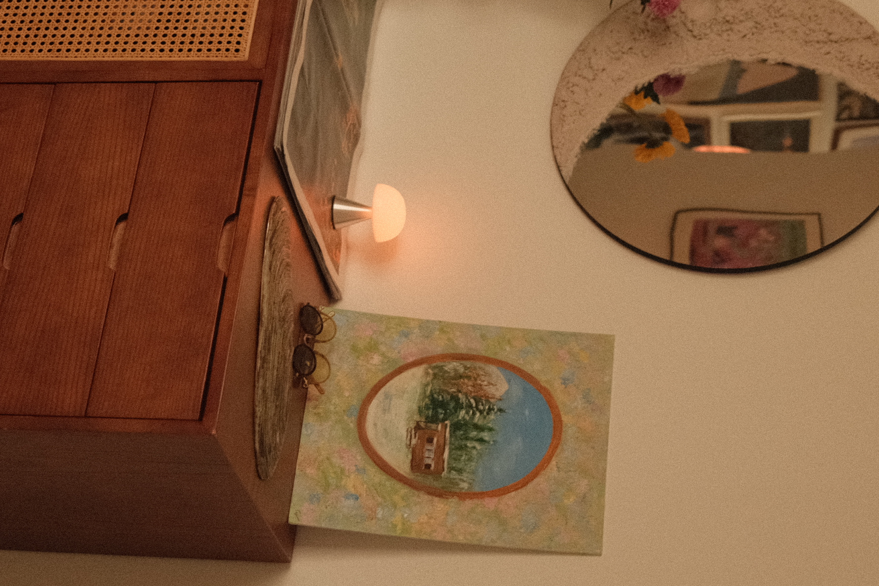 The tiny entryway to our heritage home - Wooden cabinet, round mirror, warm light, framed picture, abstract painting