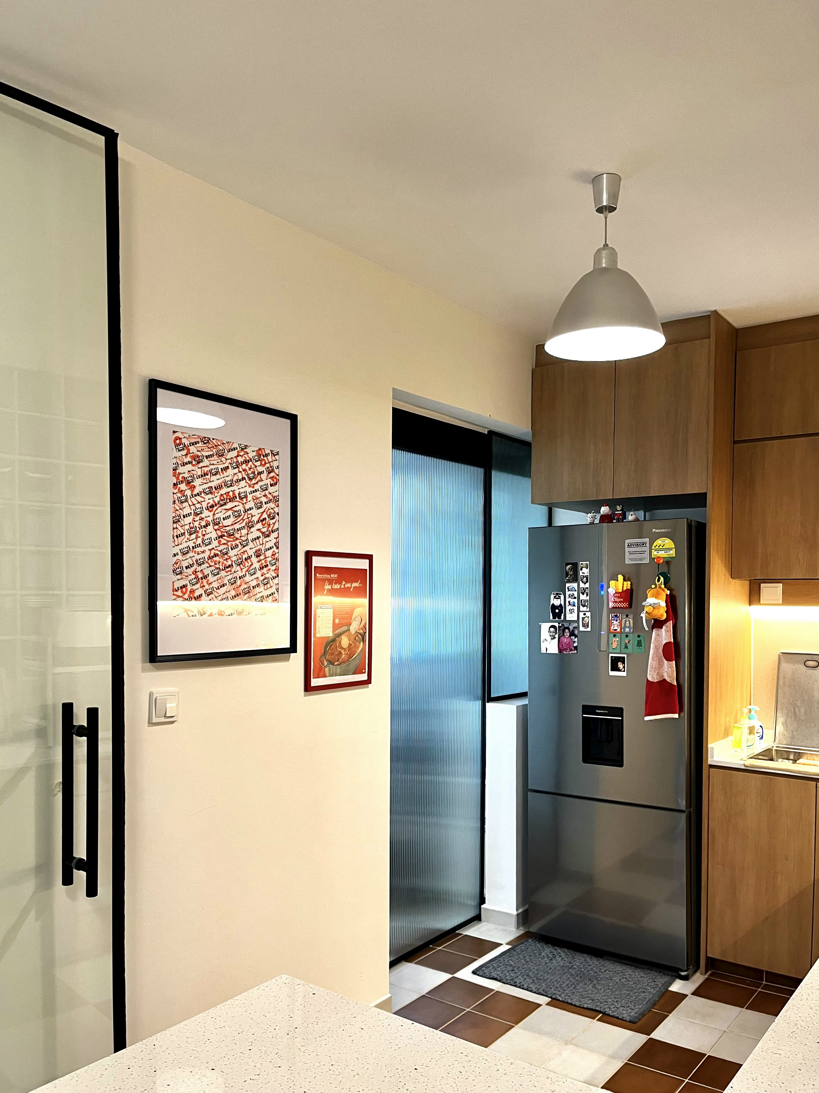 A retro and playful home - Modern kitchen with stainless steel refrigerator, wooden cabinets, tiled floor, framed artwork on