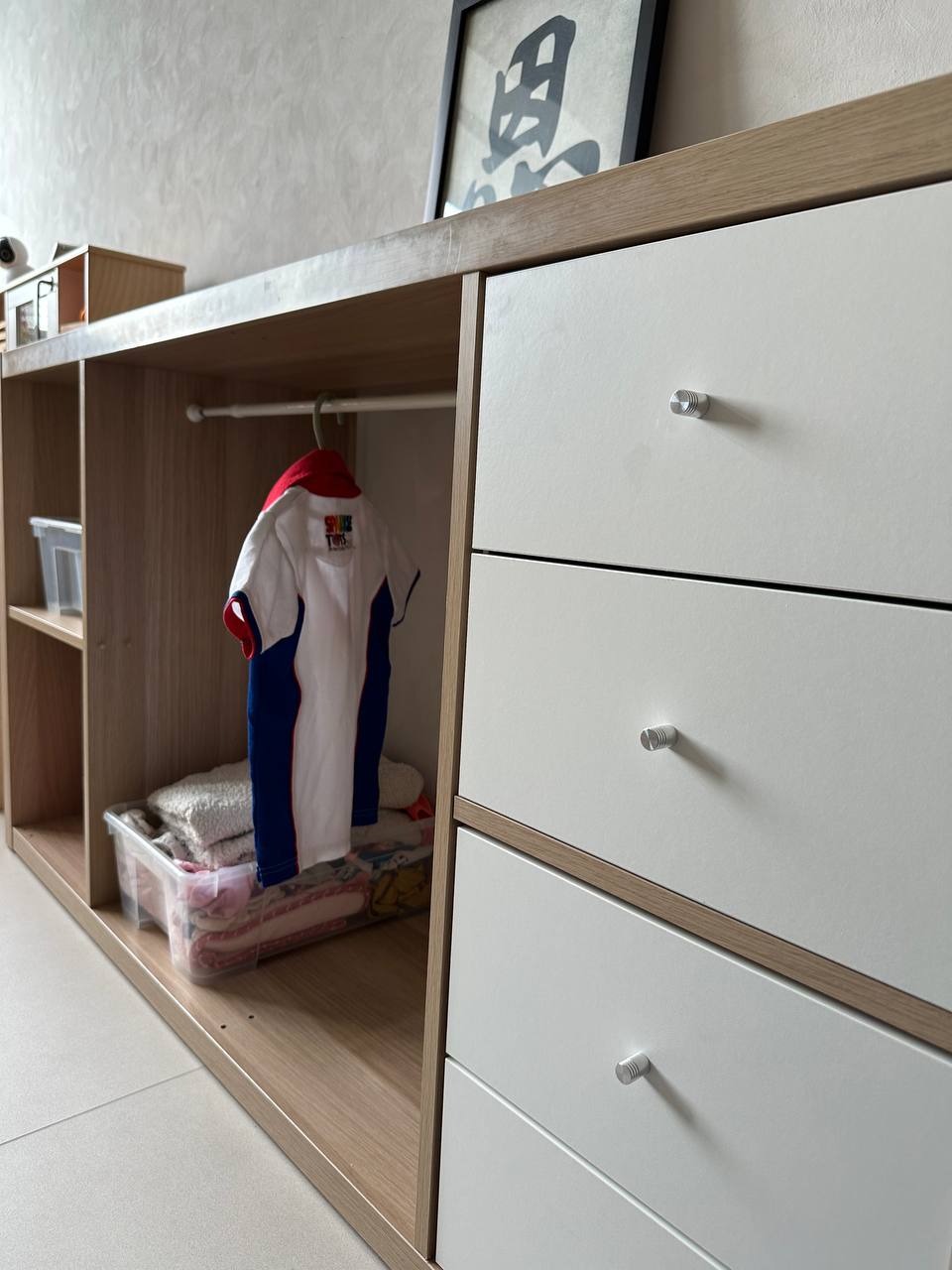 A modern minimalist inspired home  - Wooden wardrobe with white drawers, child's sports jersey hanging on rod, neatly folded