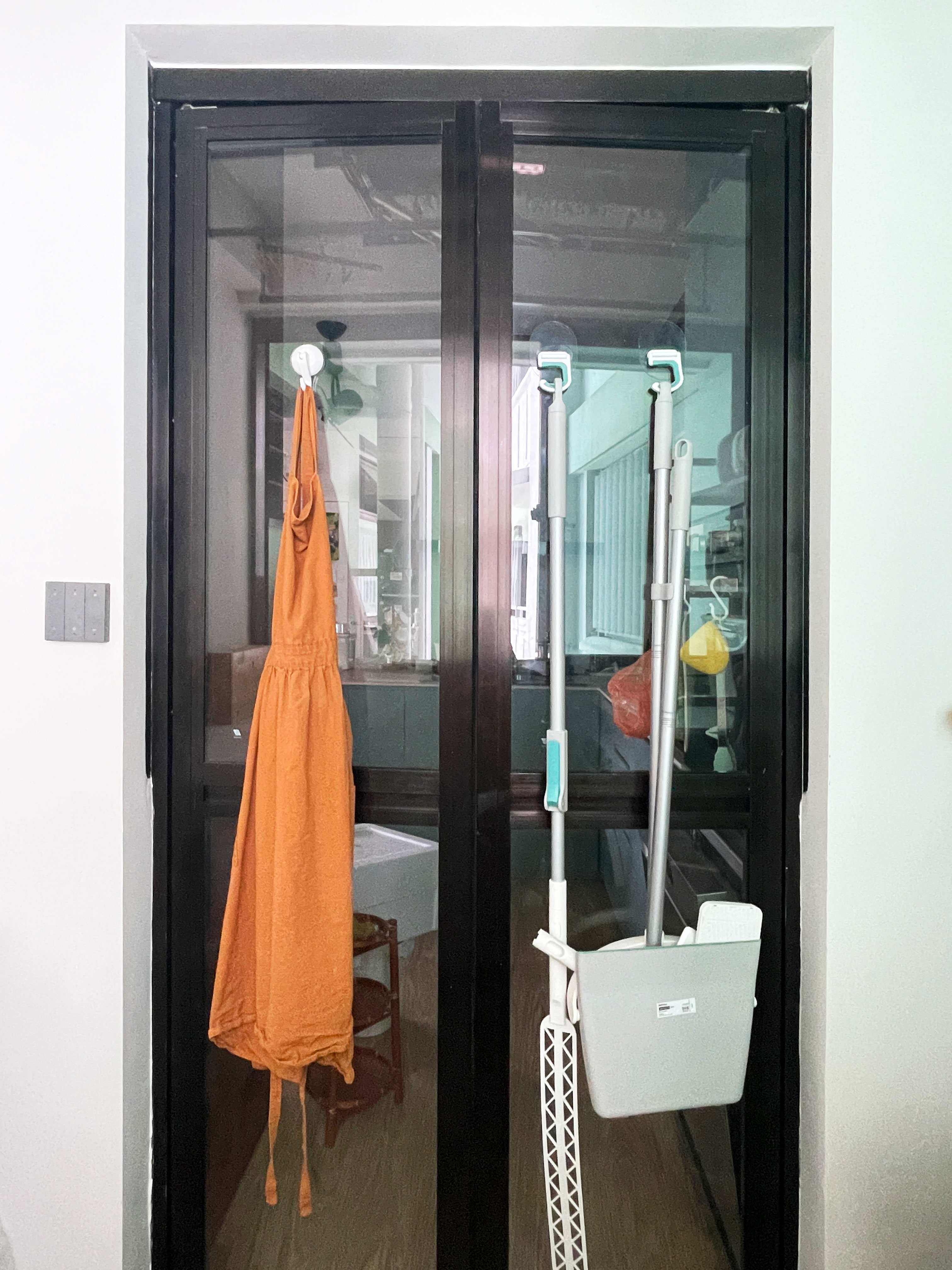 Maximising storage in a tiny service yard  - Glass door, orange apron, cleaning tools, white dustpan, black frame, indoor