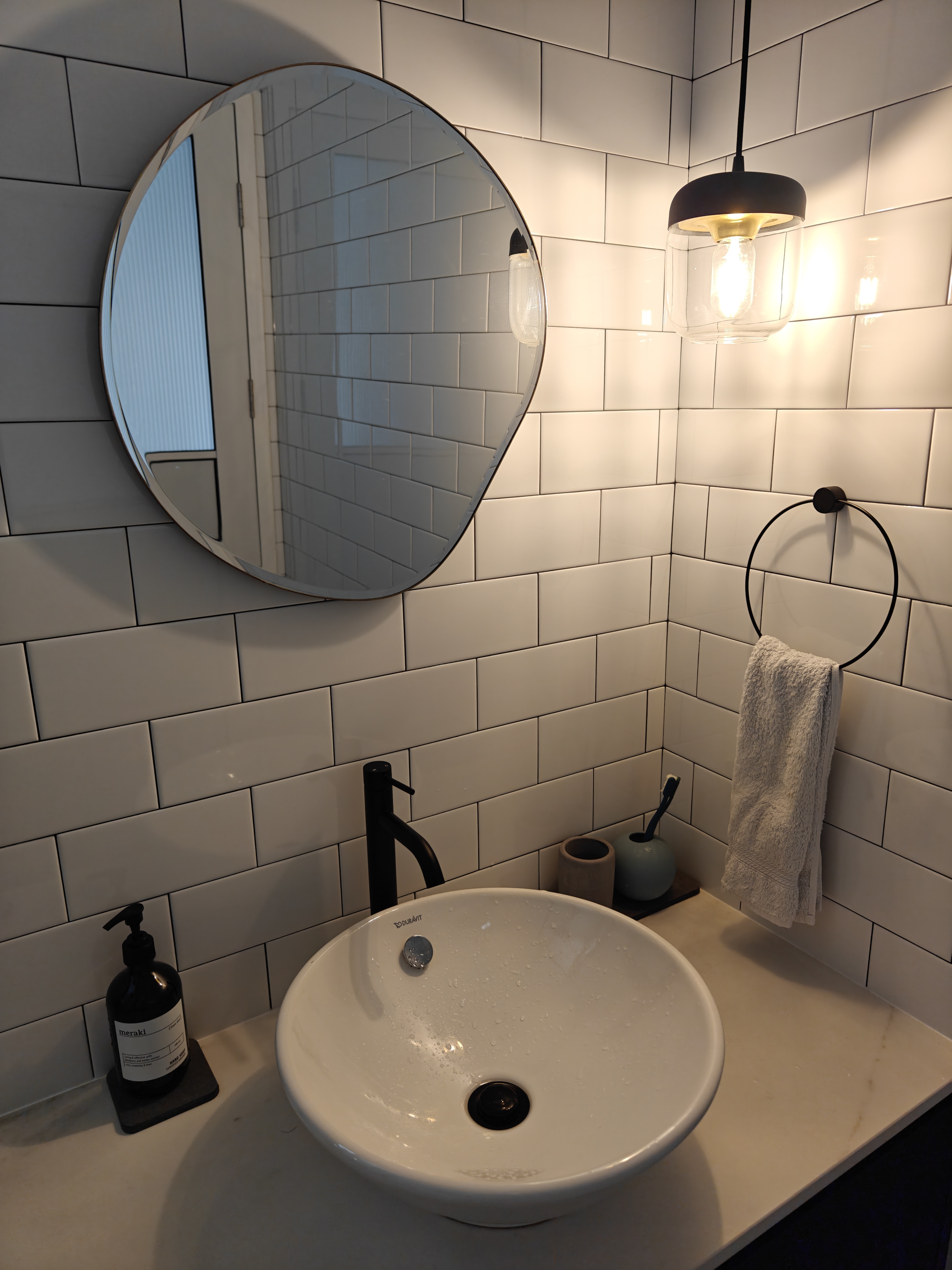 A 3-Gen Scandinavian Home - Modern bathroom with white tiled walls, sleek black faucet, black soap dispenser, white oval