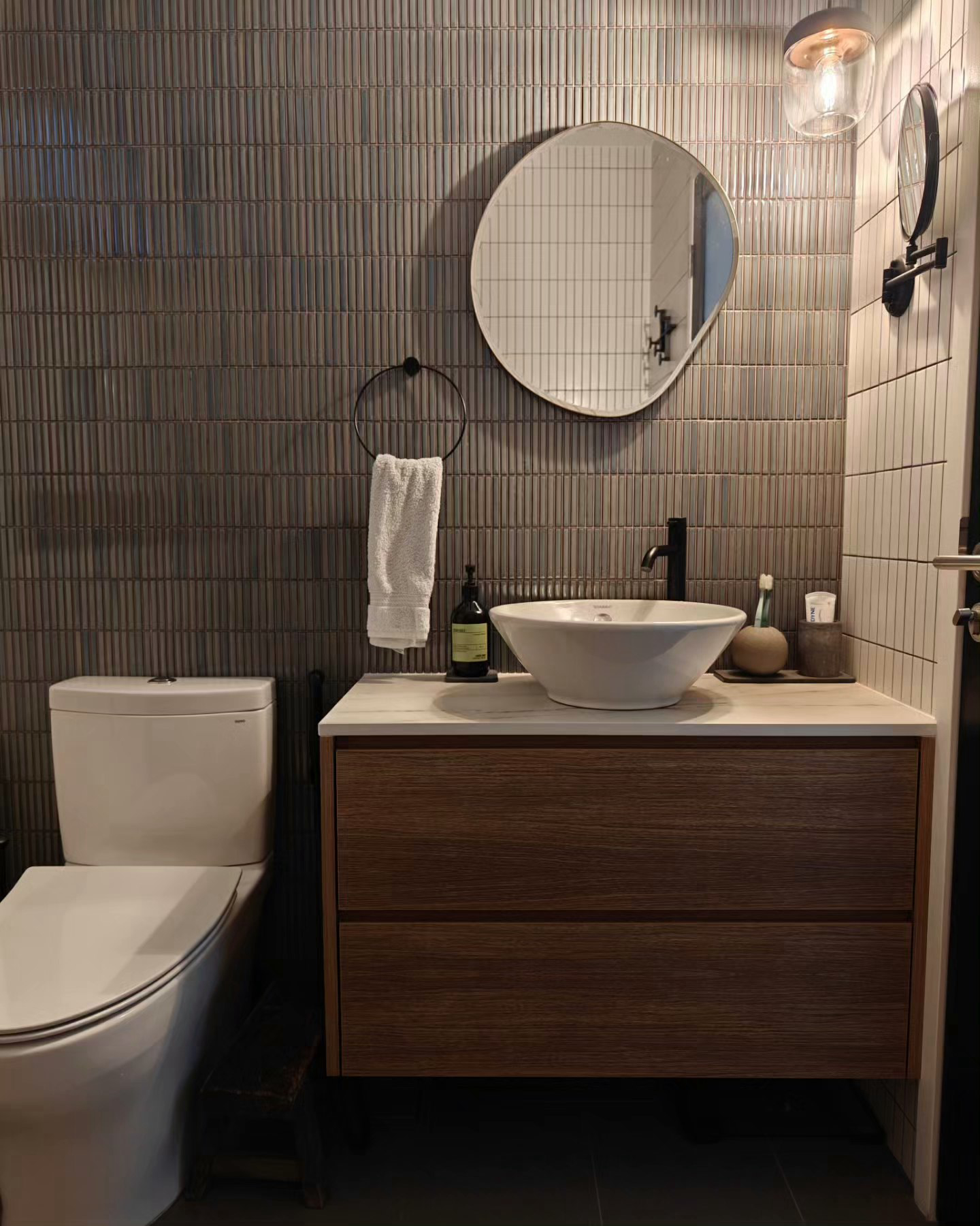 A 3-Gen Scandinavian Home - Modern bathroom with sleek design, beige toilet, wooden vanity, round mirror, white sink, black