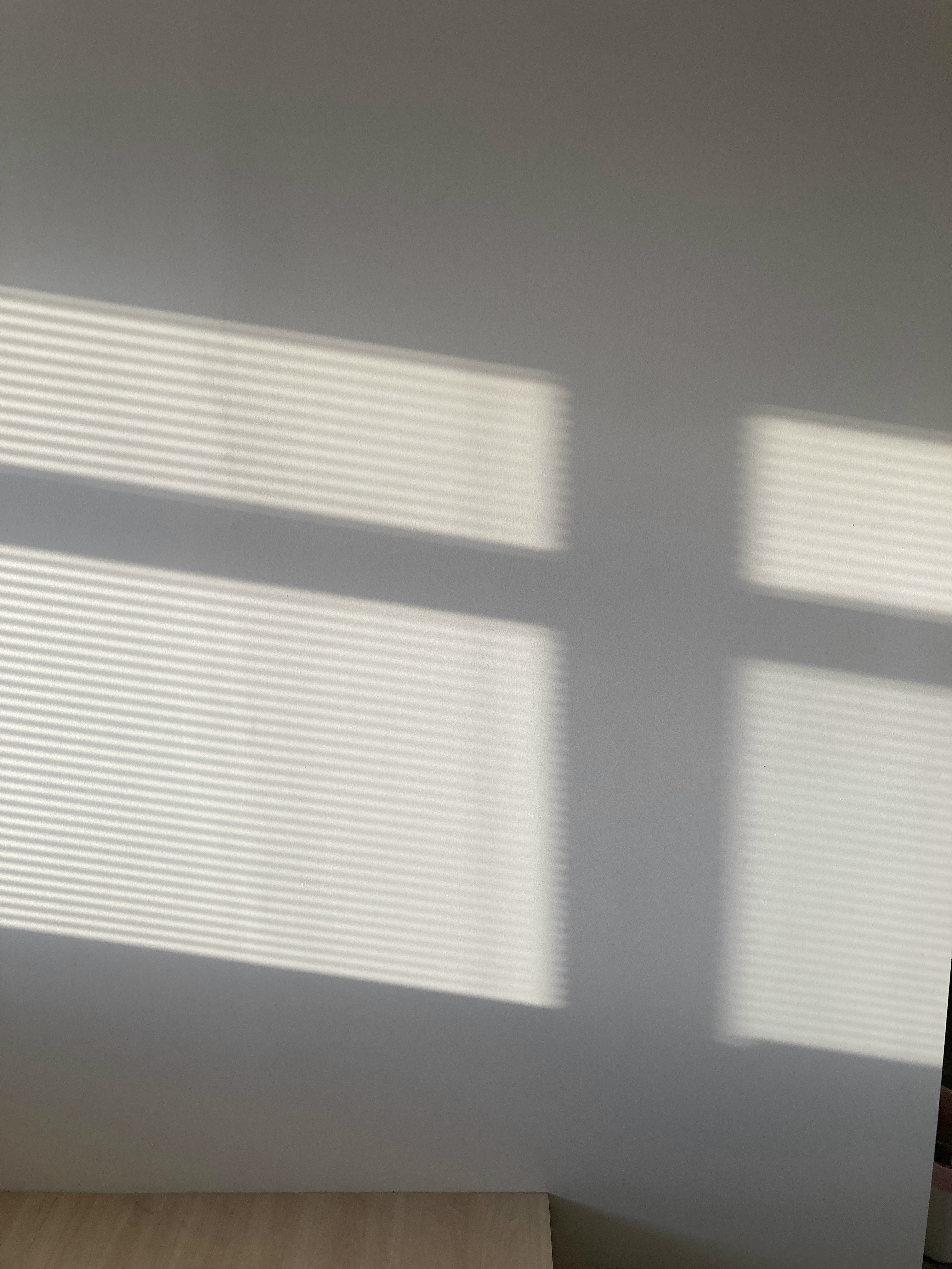 Day vs Night - Illuminating our home - Sunlight streaming through blinds, casting shadows on a white wall, creating a striped