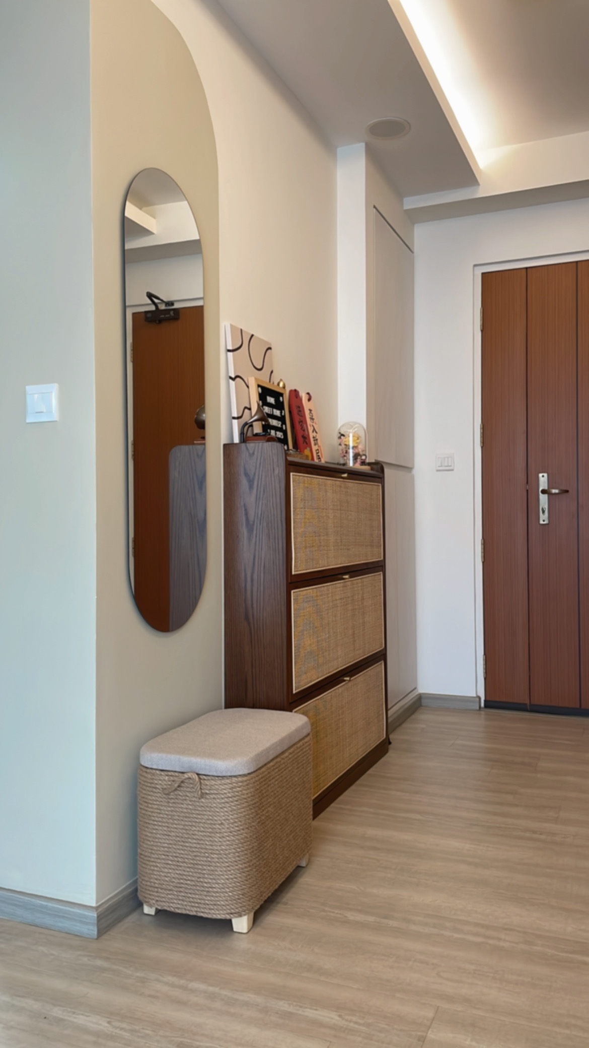 Our cosy crib filled with rattan-wooden accent pieces  - Wooden floor, light-colored walls, arched mirror, woven ottoman