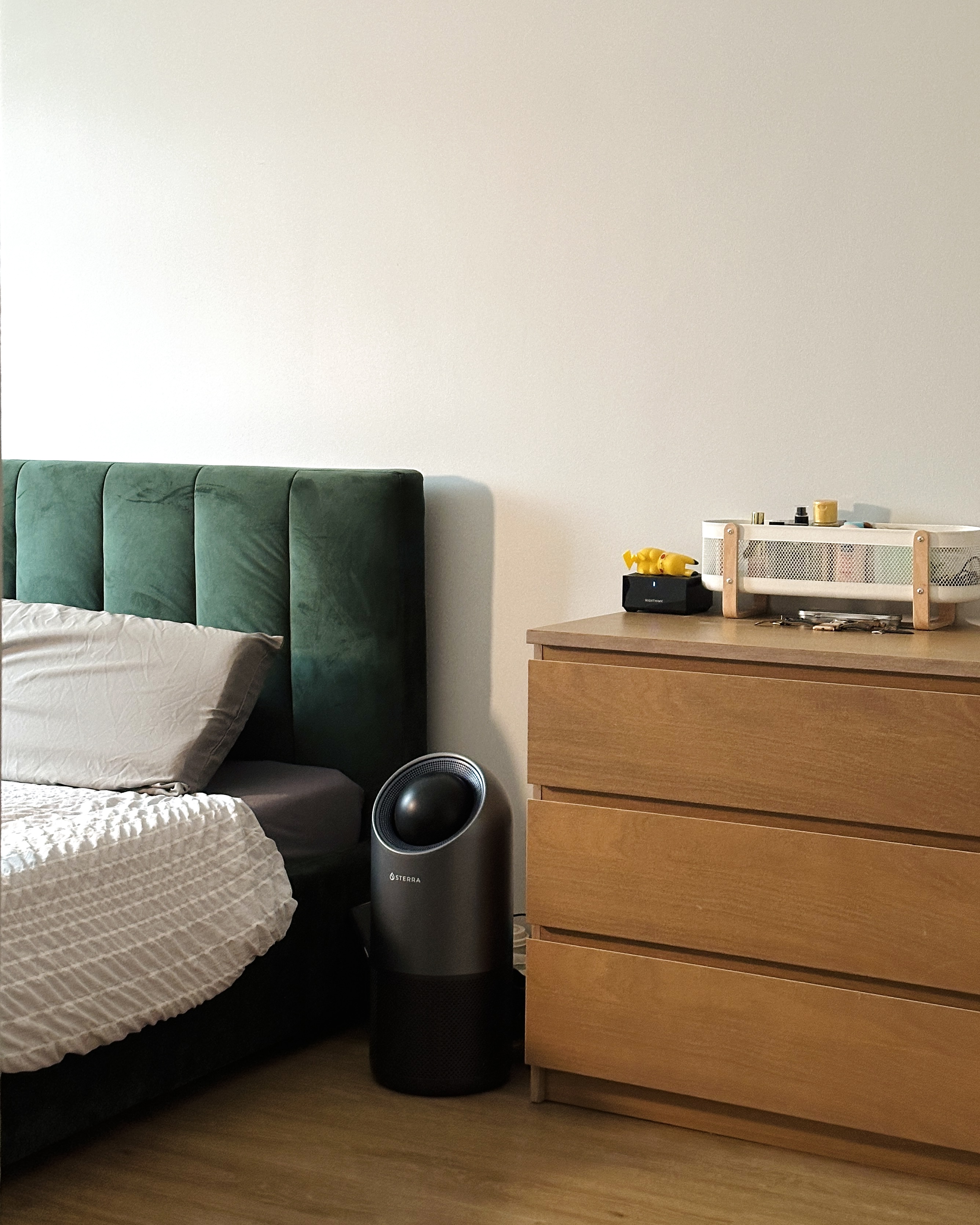 A house of quirks - Green upholstered headboard, white and gray bedding, modern bedside table, black and gray air purifier
