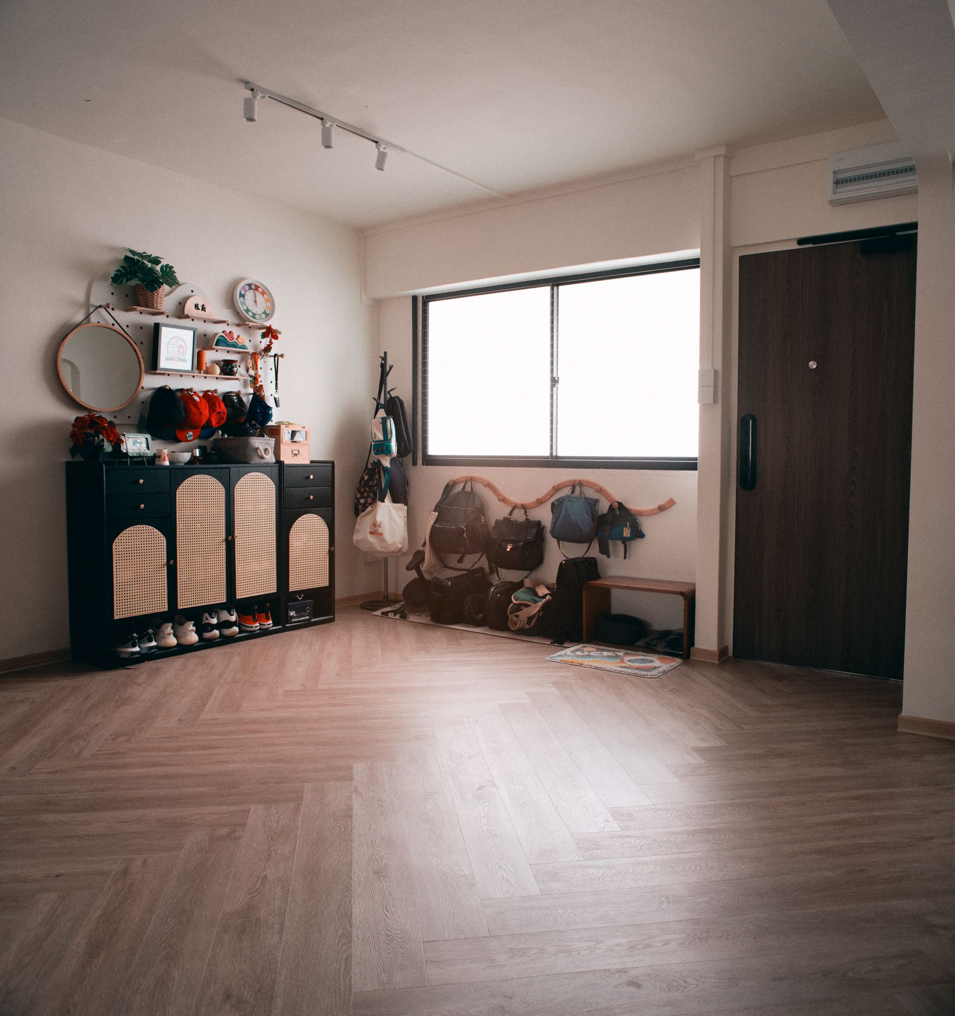 An entryway built around family habits - Wooden floor, black dresser, shoes, mirror, clock, plants, wall decorations, hanging