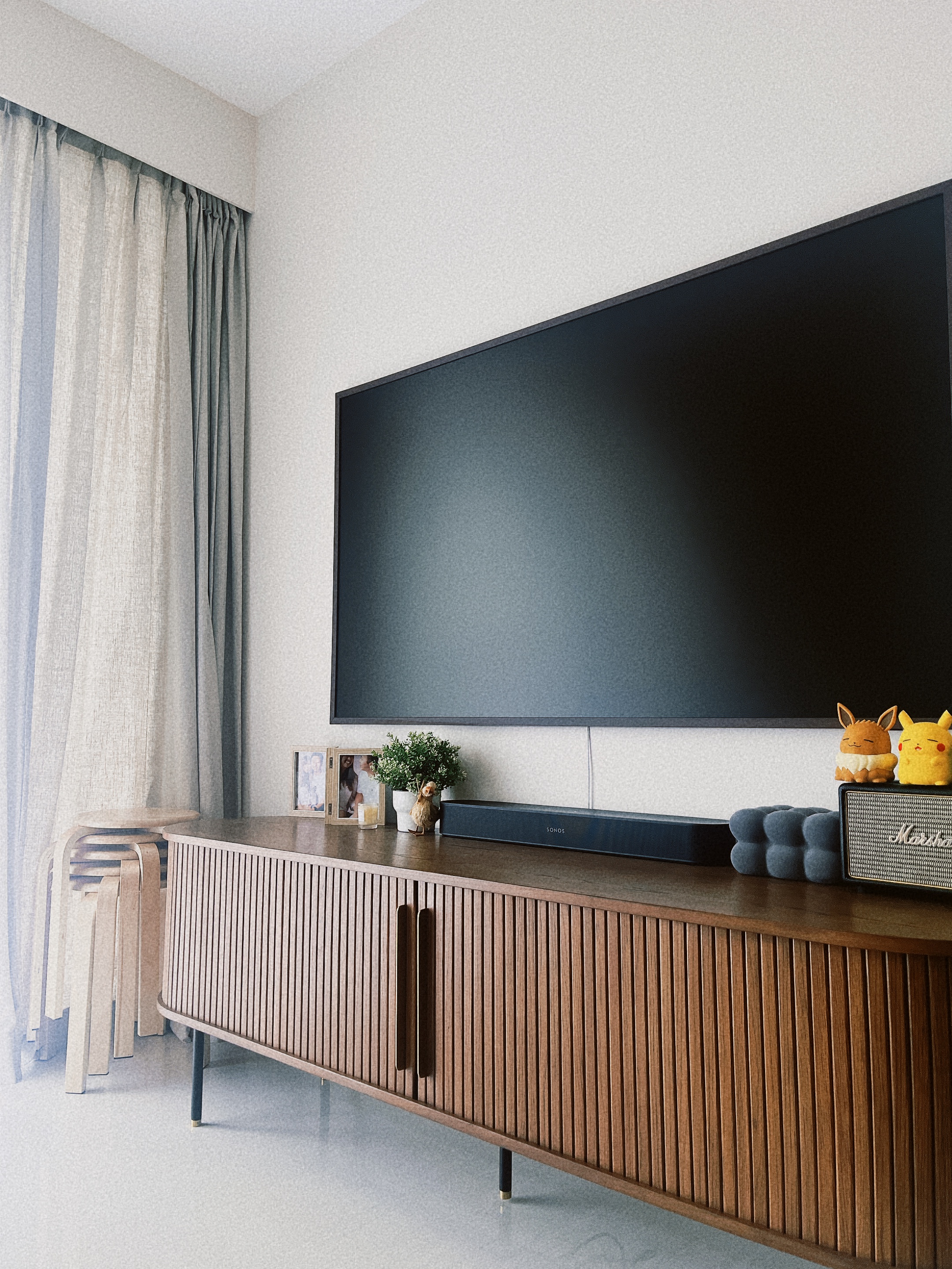 Our WIP 2+S Home - Large flat-screen TV, minimalist decor, wooden console, soft natural light, light gray curtains, wooden