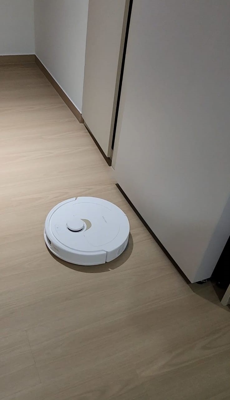 Minimalist Monopoly.home - White robotic vacuum cleaner on light wooden floor, near closed white door, minimalistic room