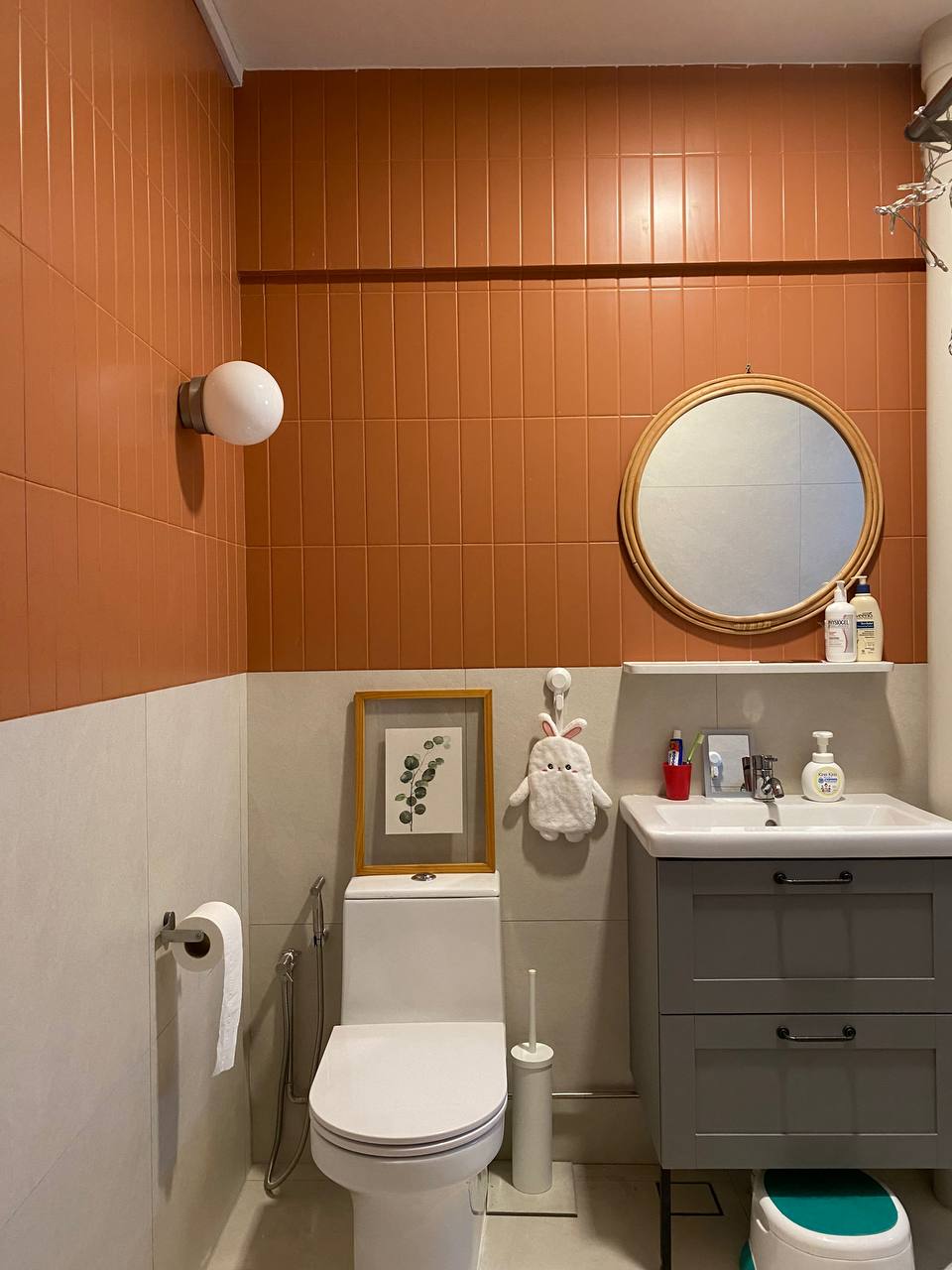 A Modern Farmhouse - Orange-tiled wall, white toilet, round mirror, white sink, gray cabinet, toilet paper holder, framed