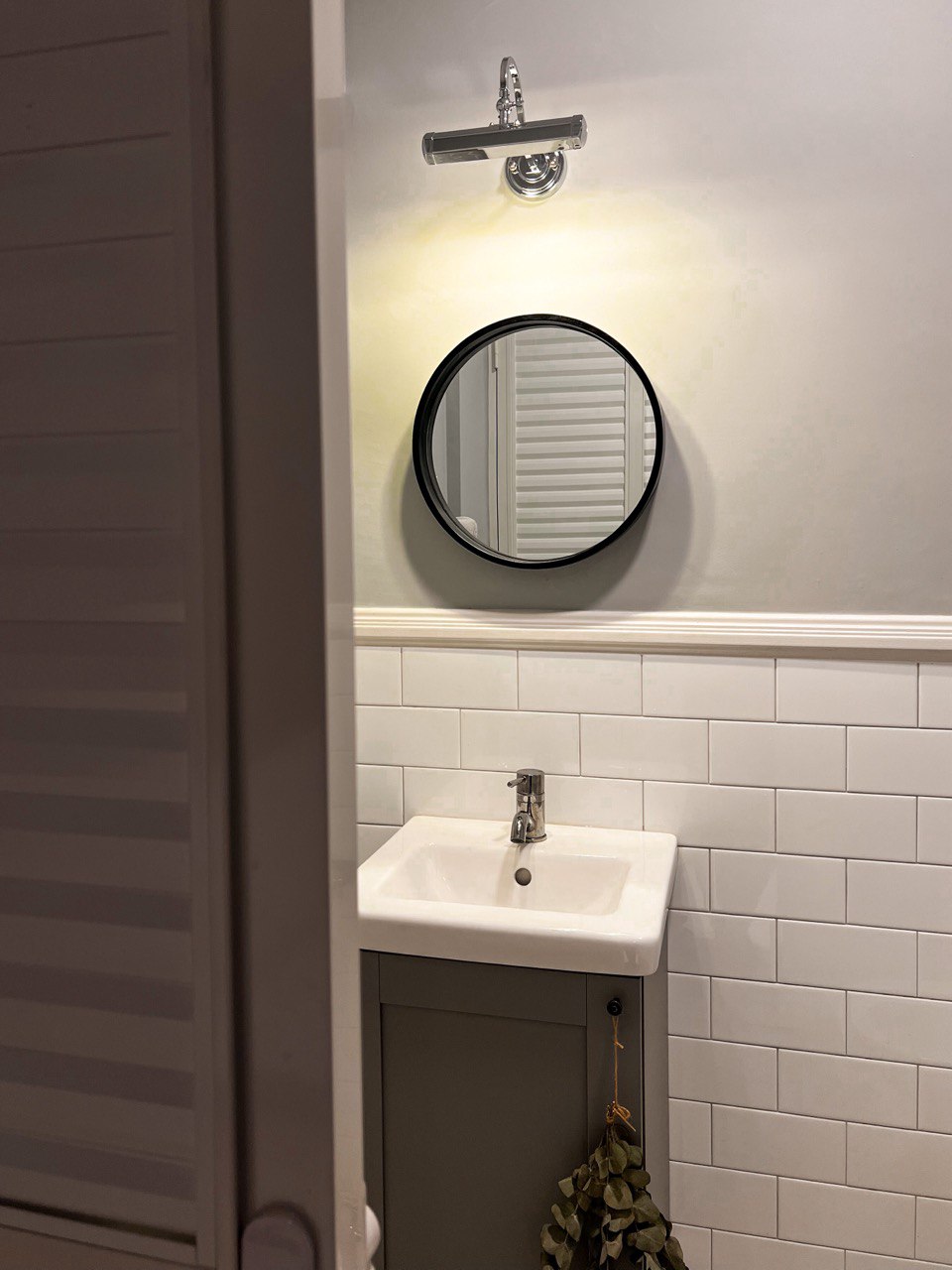A Modern Farmhouse - Round mirror with black frame, white tiled wall, white sink, silver faucet, light fixture above mirror