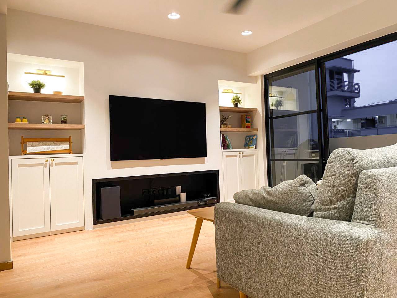 A Modern Farmhouse - Modern living room with large flat-screen TV, minimalist decor, light wood flooring, cozy gray sofa