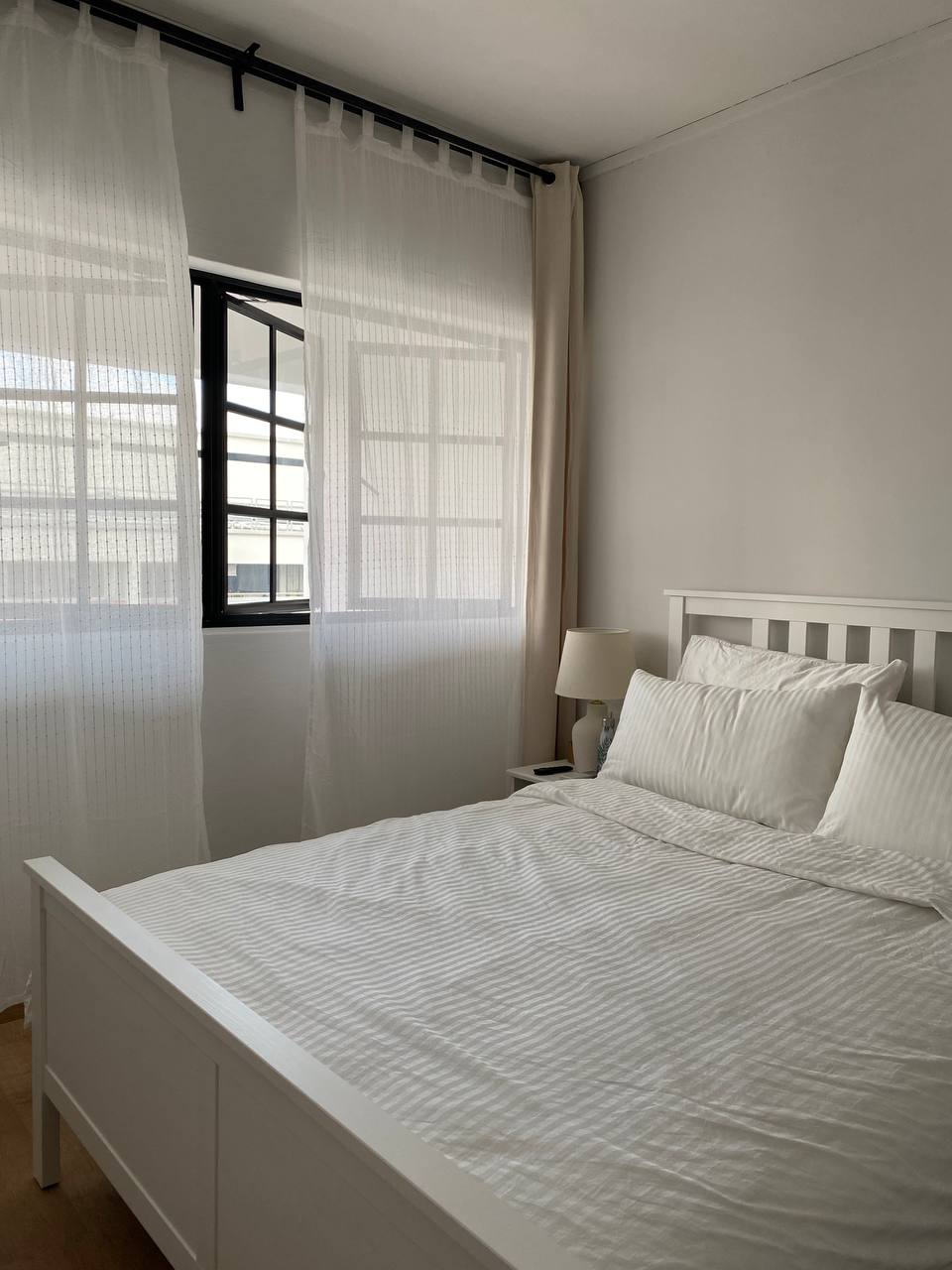 A Modern Farmhouse - White bed with striped bedding, sheer curtains, minimalist bedside table, modern window with black