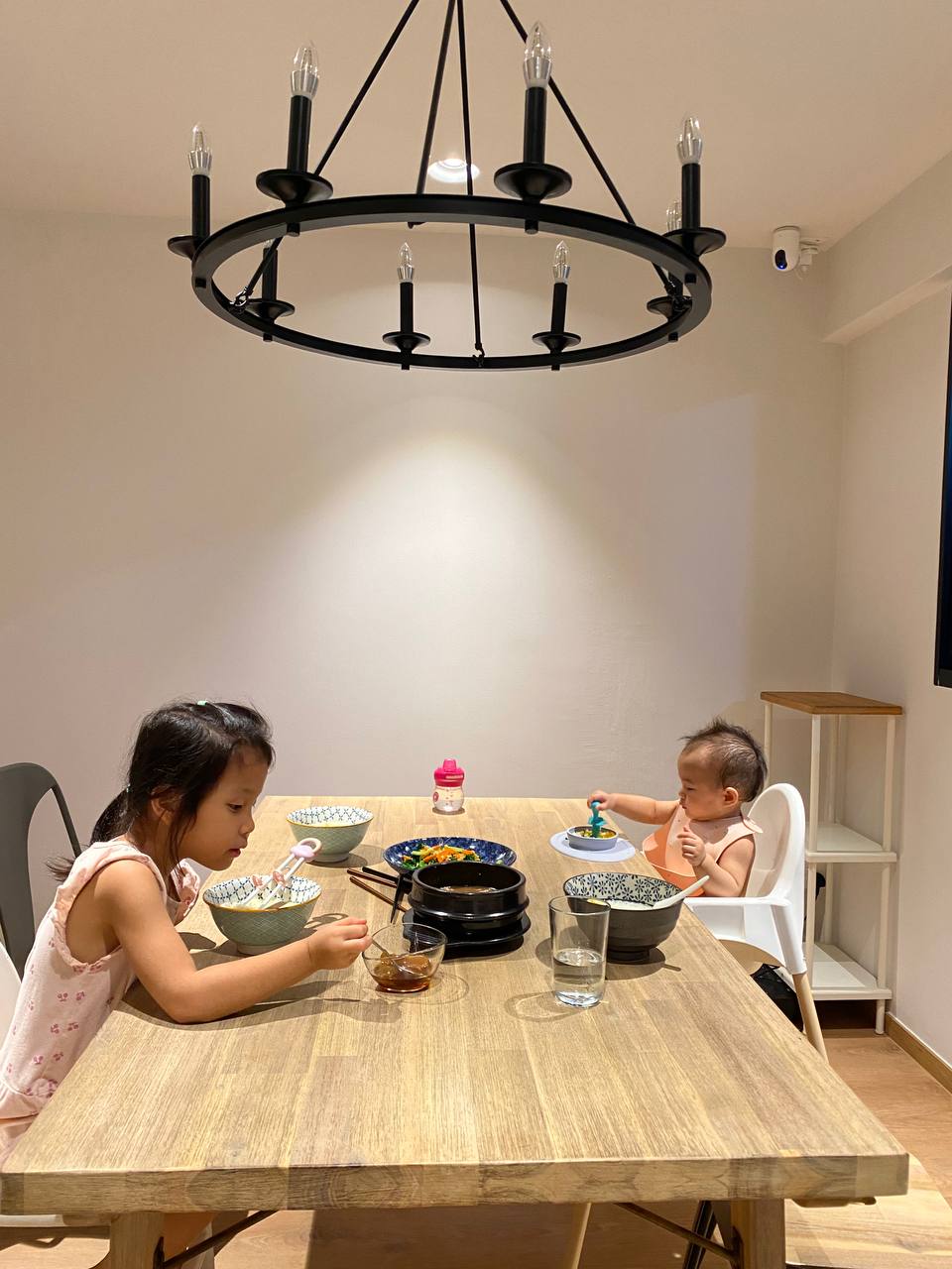 A Modern Farmhouse - Children enjoying mealtime, young girl eating, toddler sitting, wooden dining table, modern chandelier